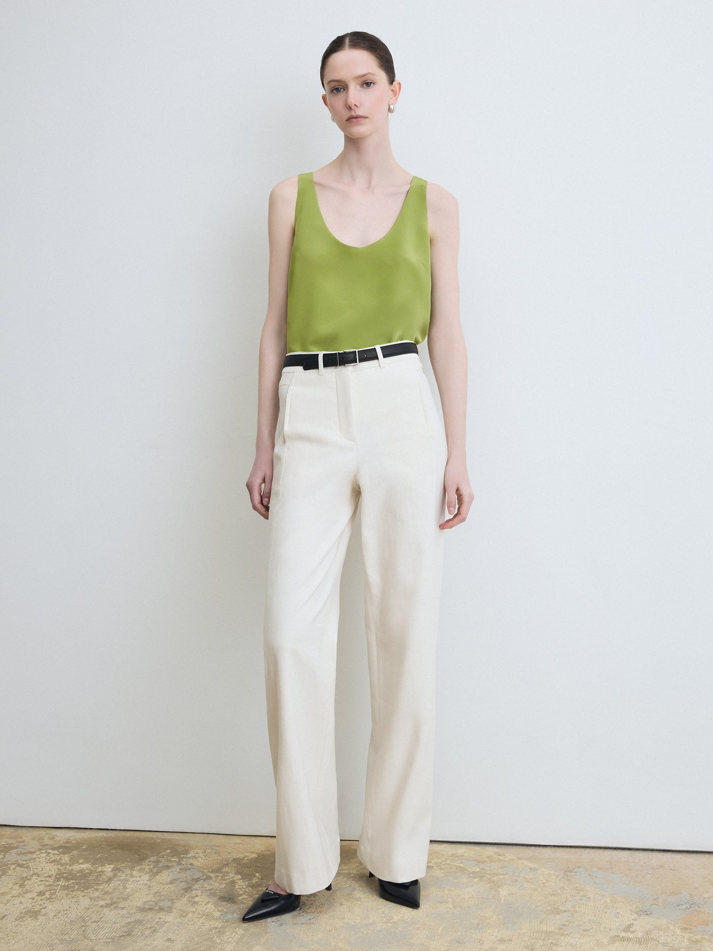 Woman wearing a green sleeveless top and beige pants against a plain background