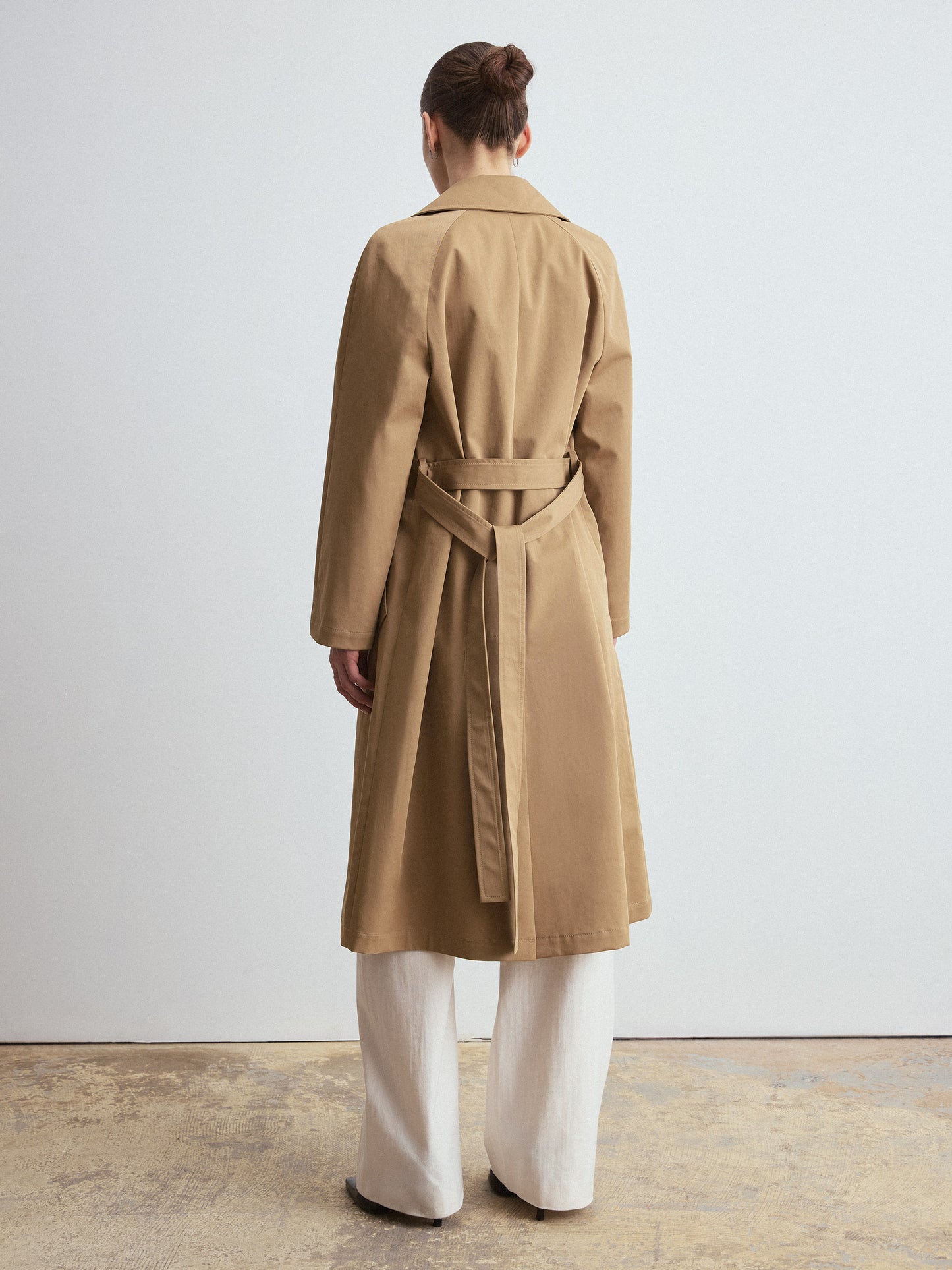 Person wearing a camel trench coat standing against a plain background