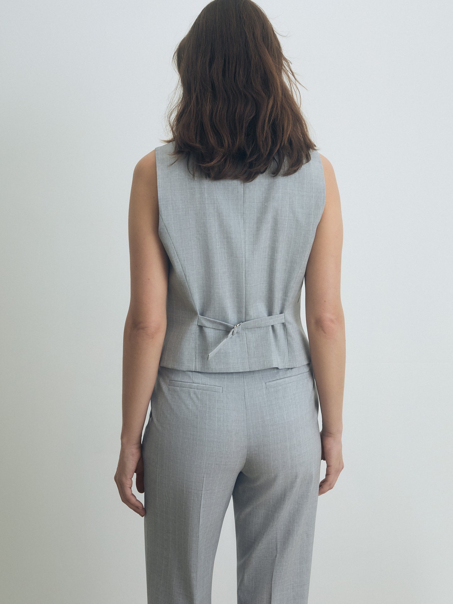 Woman wearing a gray sleeveless vest and pants set on a plain background