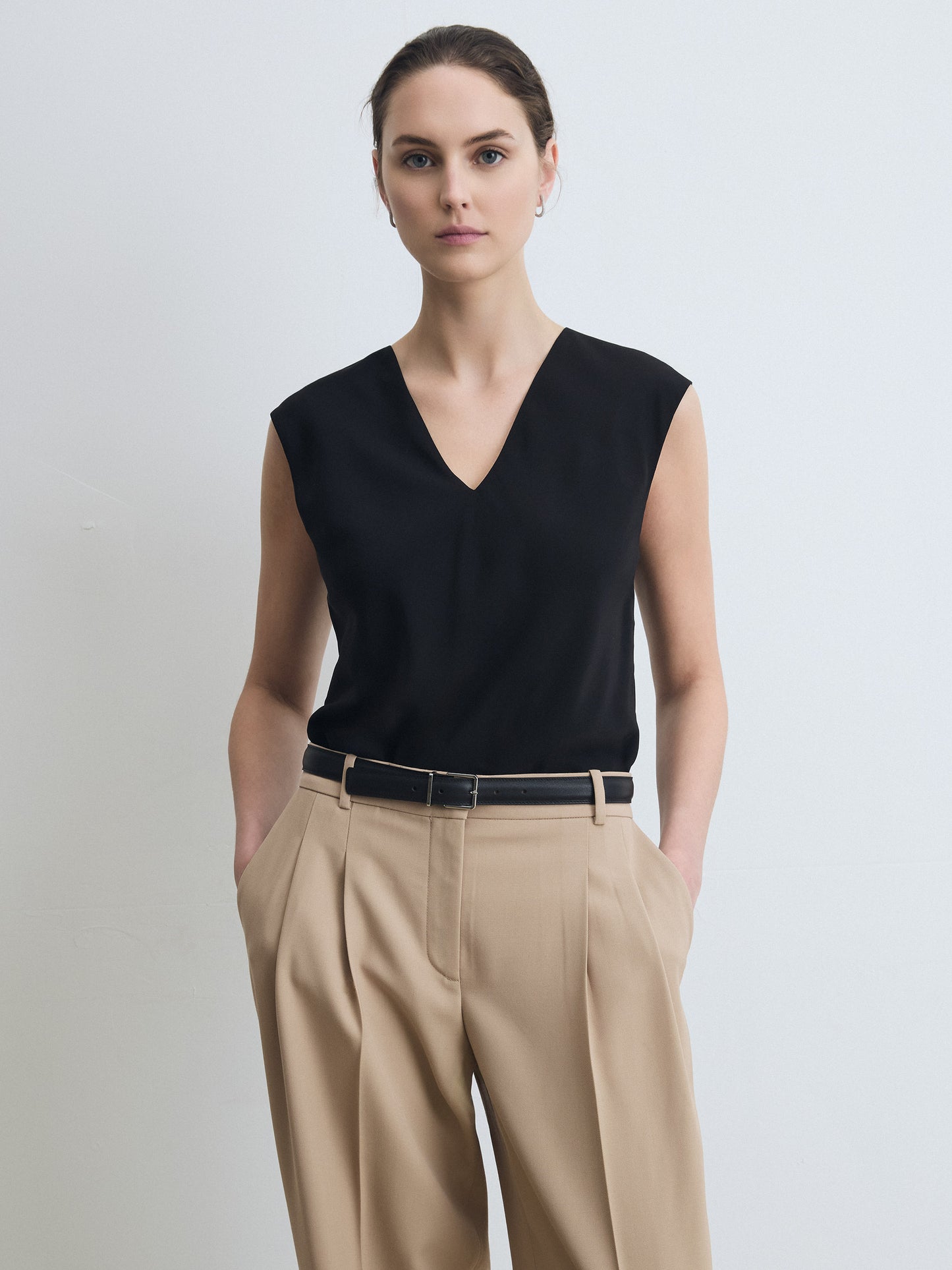Woman wearing a black sleeveless top and beige pants against a light background