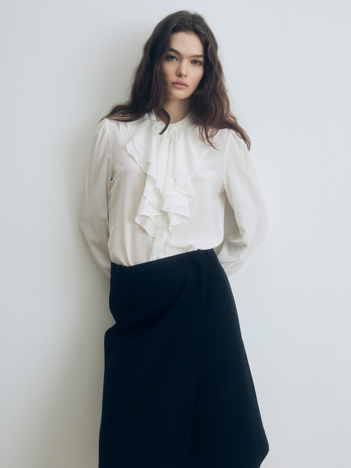 Woman wearing a white blouse with ruffles and a black skirt against a plain background