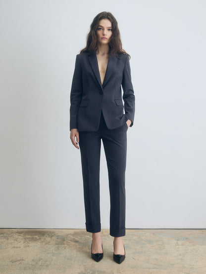 Woman wearing a dark grey suit standing against a plain background