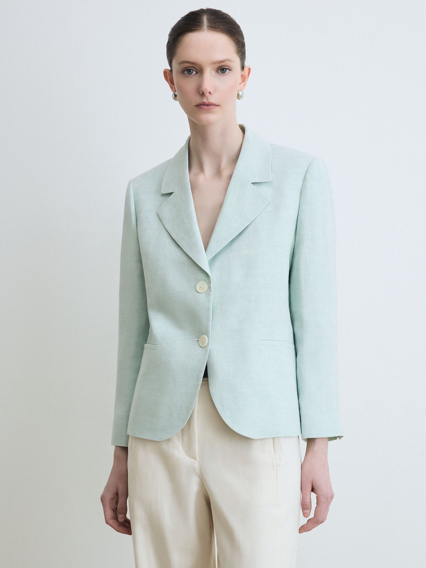 Person wearing a light blue blazer and beige pants on a plain background