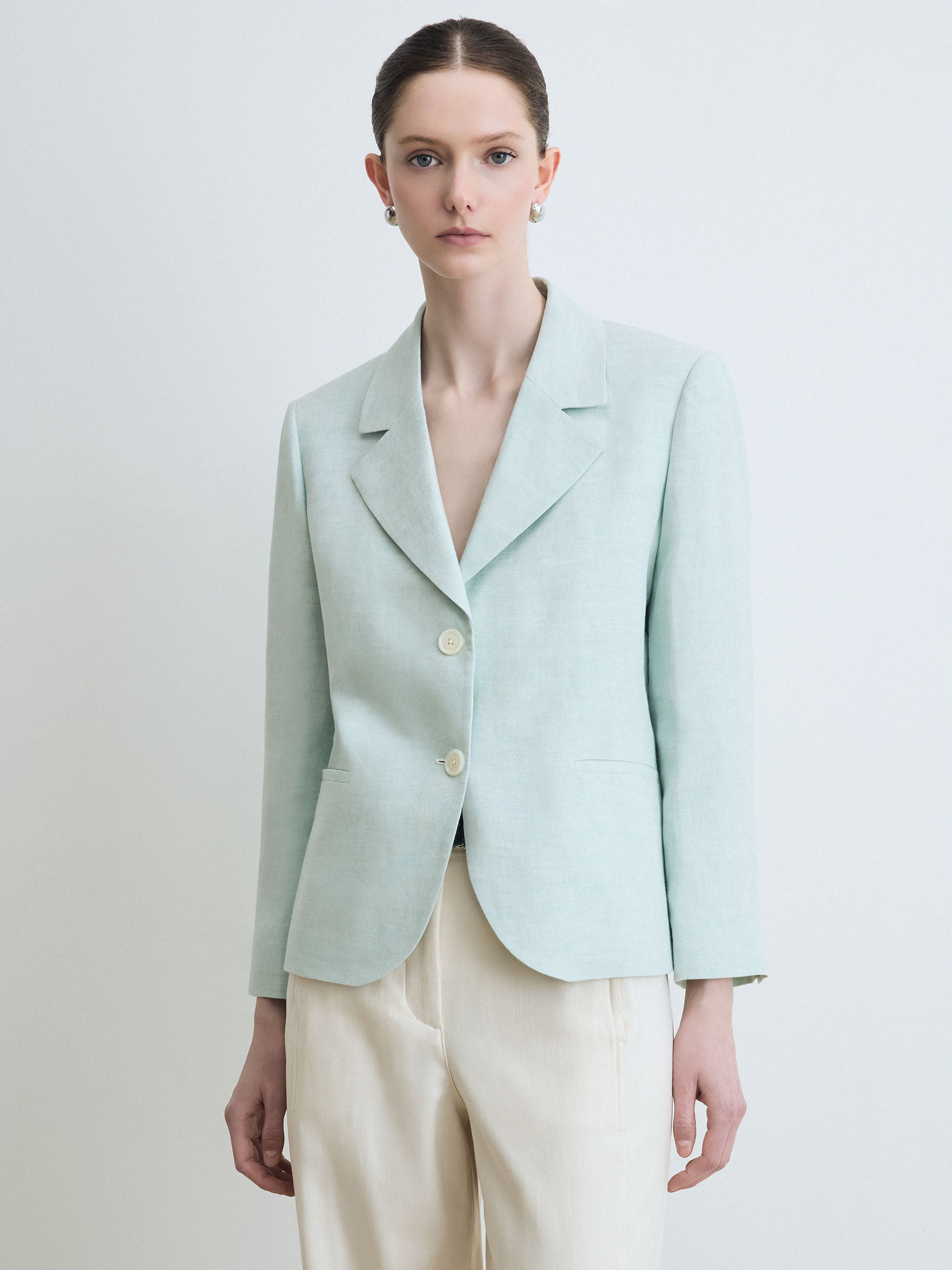 Person wearing a light blue blazer and beige pants on a plain background