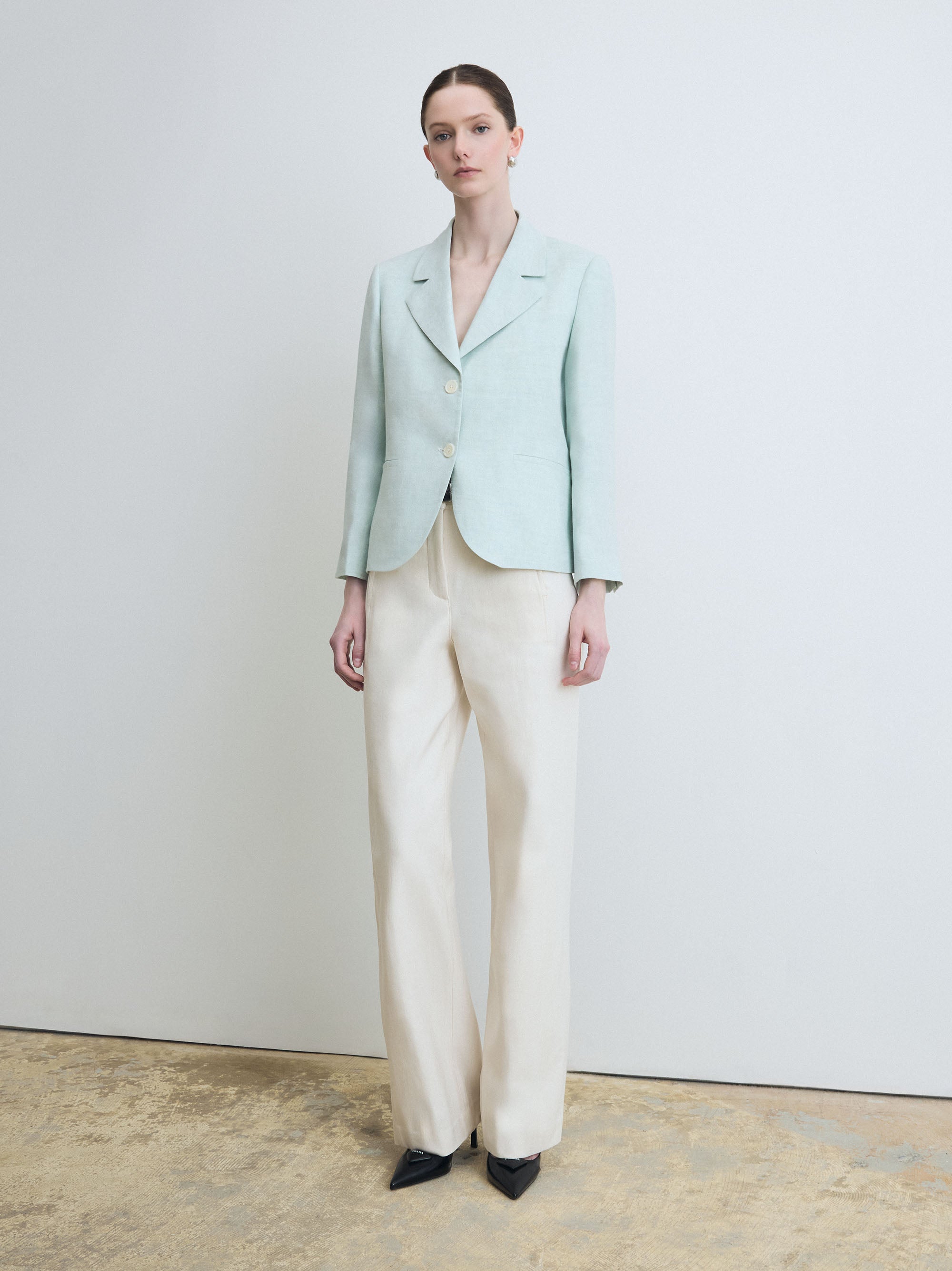 Woman wearing a light green blazer and white pants against a plain background