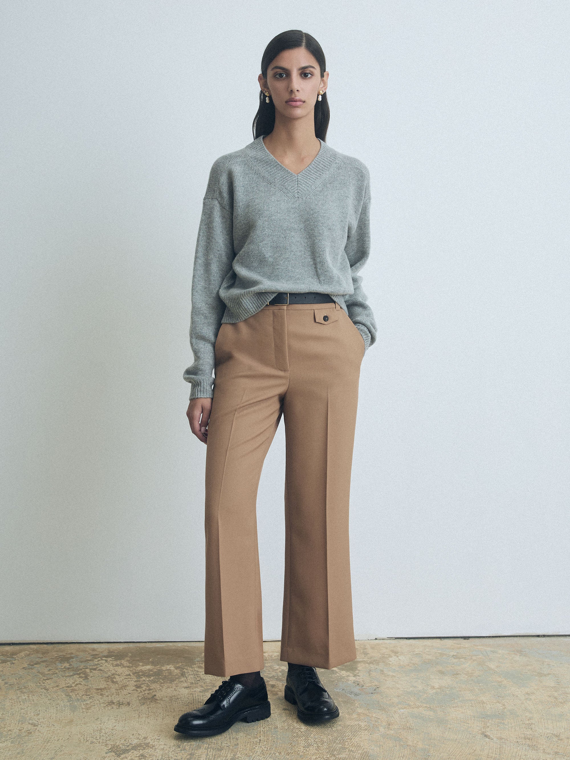 Person wearing a gray judith and charles sweater and beige pants against a plain background