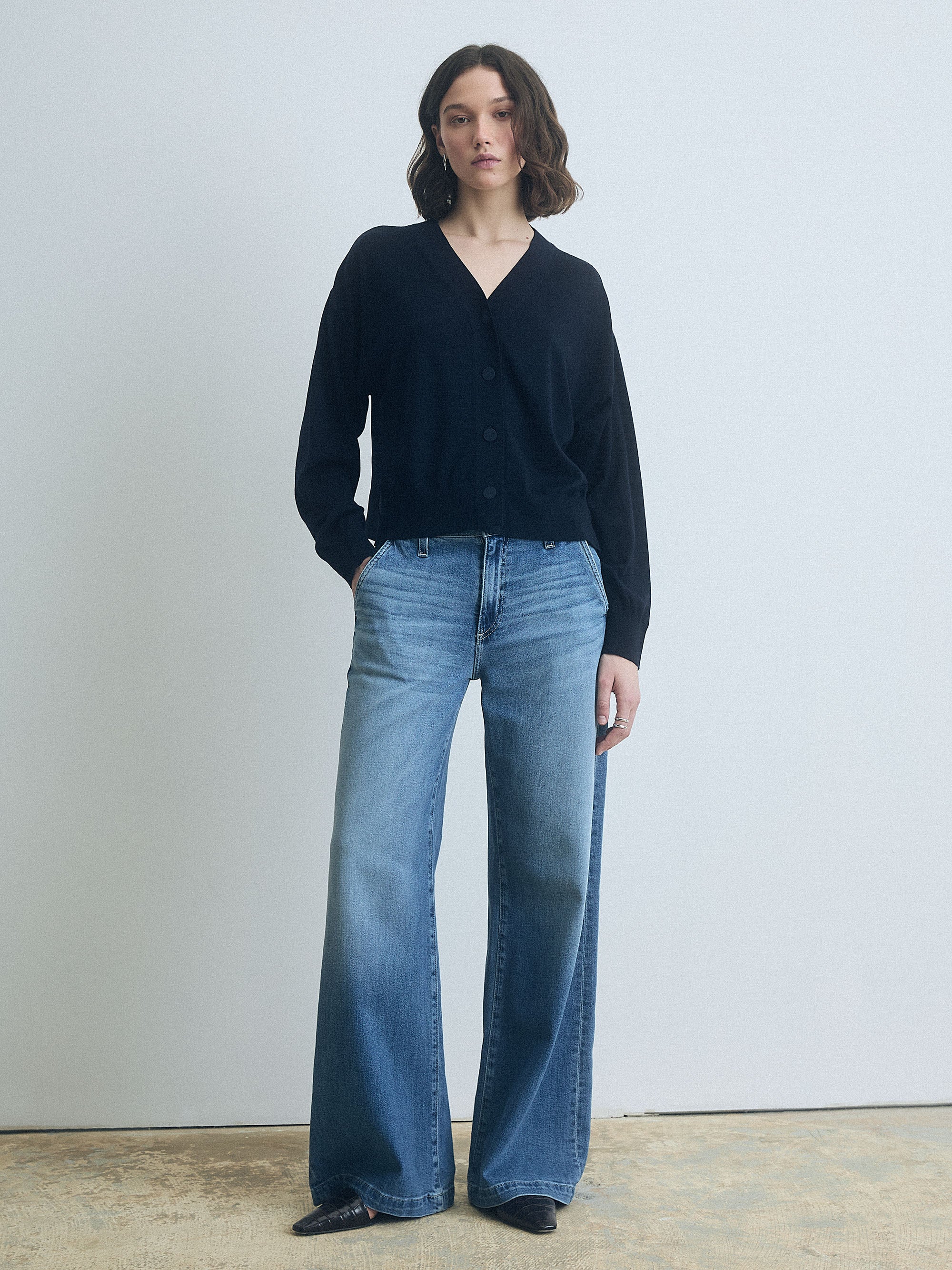 Woman wearing a Navy Boxy Silk Back Cardigan by Judith & Charles and blue jeans against a plain background