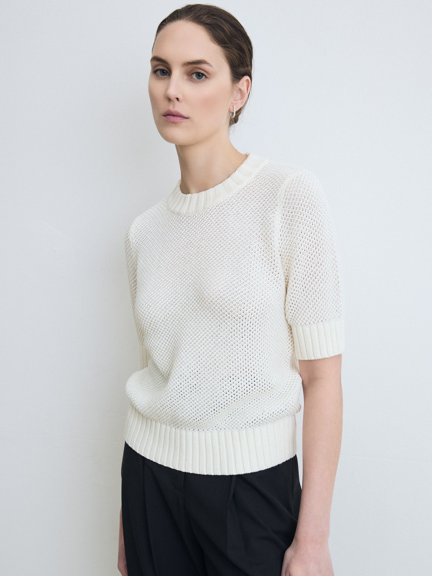 Woman wearing a white knit sweater against a plain background