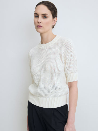 Woman wearing a white knit sweater against a plain background