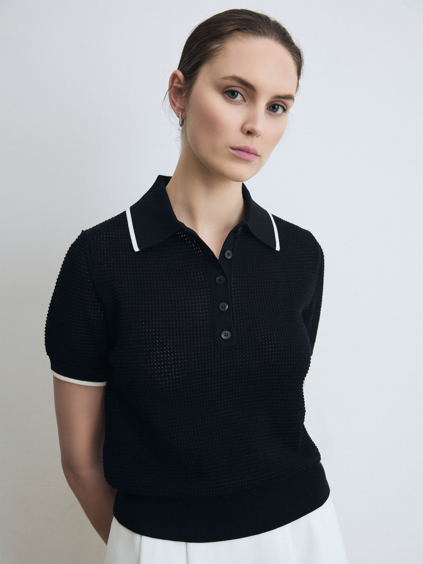 Woman wearing a black textured polo shirt with white trim on a plain background