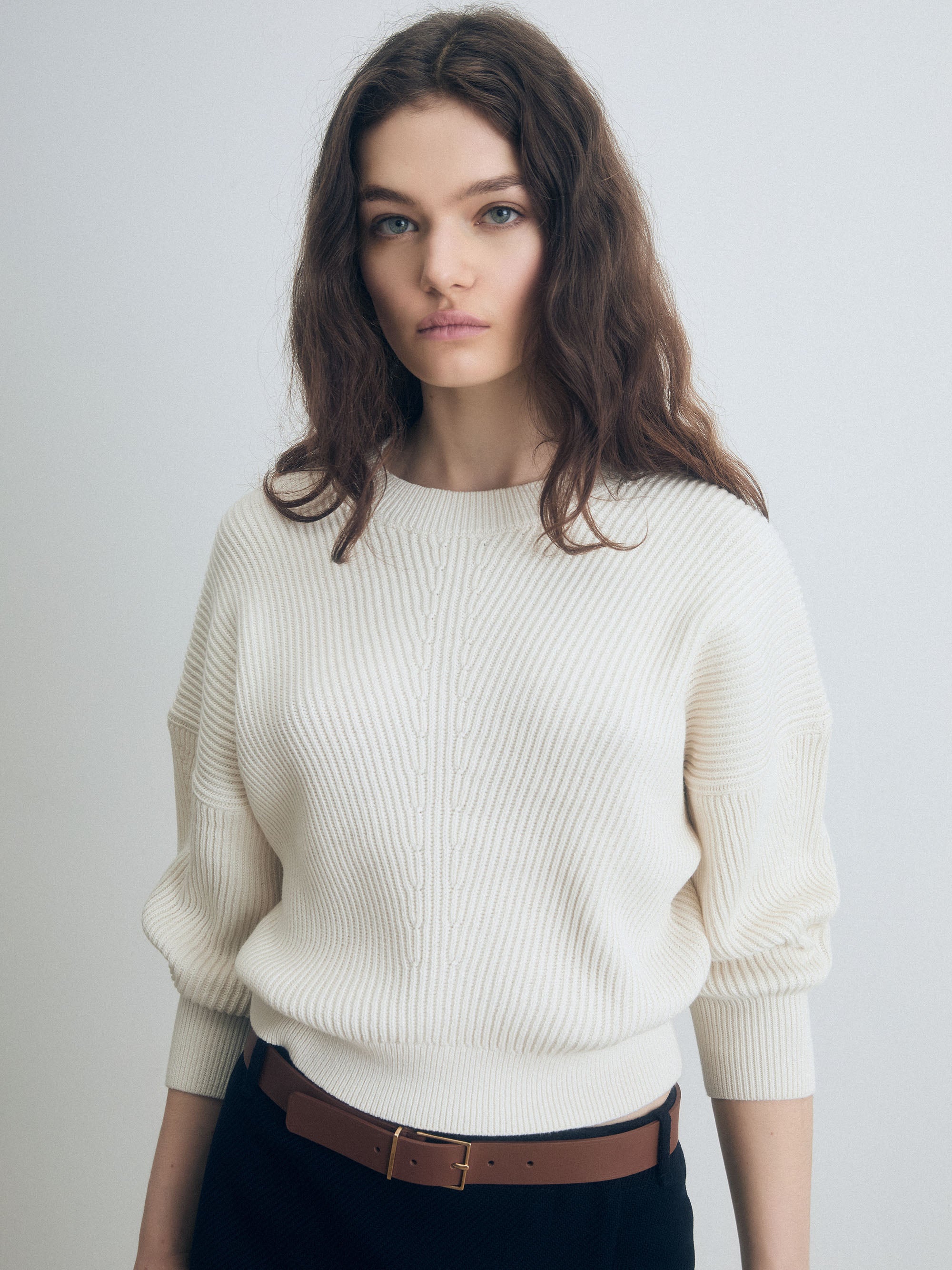 Woman wearing a white sweater with a skirt on a plain background