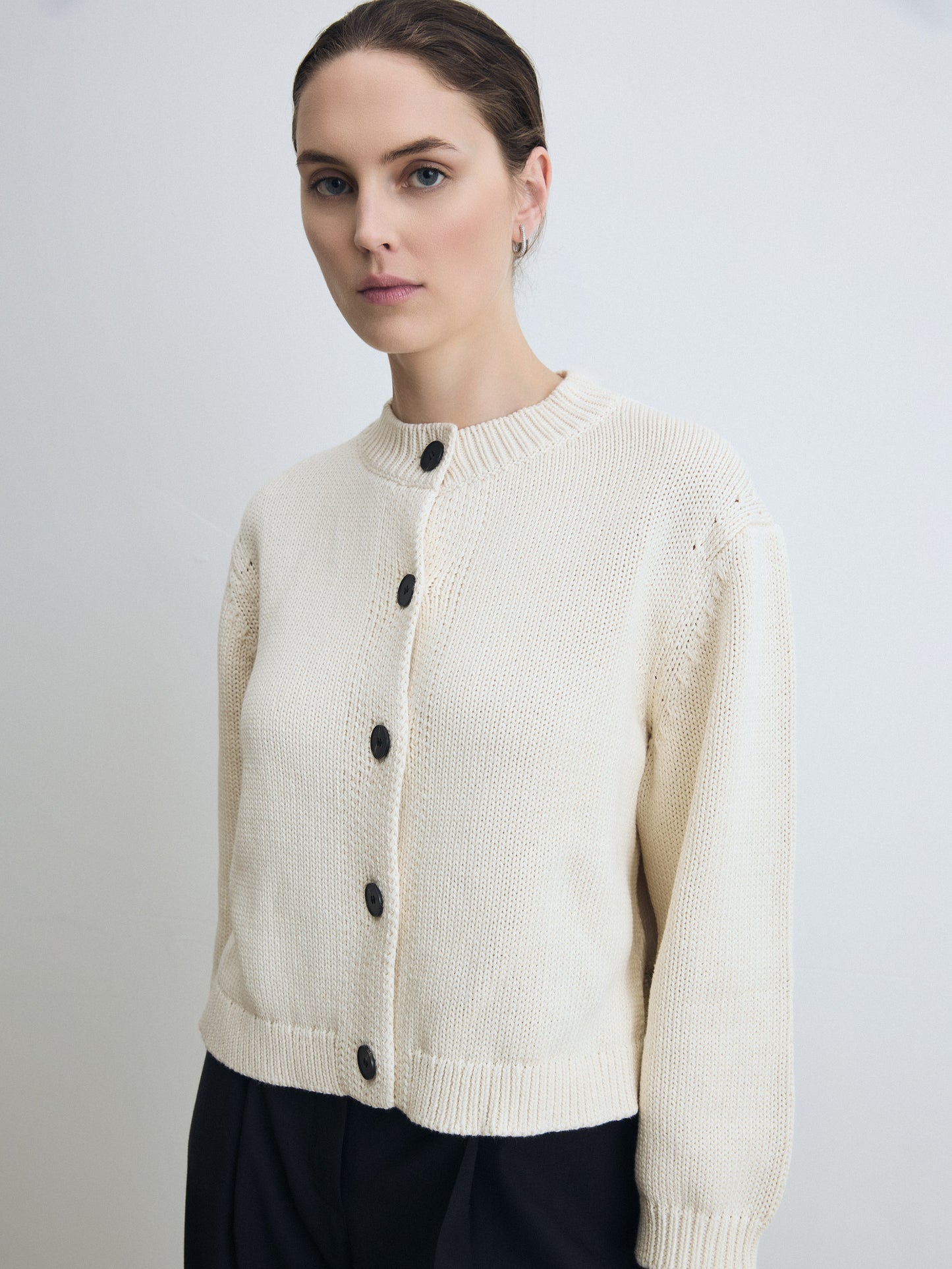 Woman wearing a pearl cardigan with black buttons on a plain background