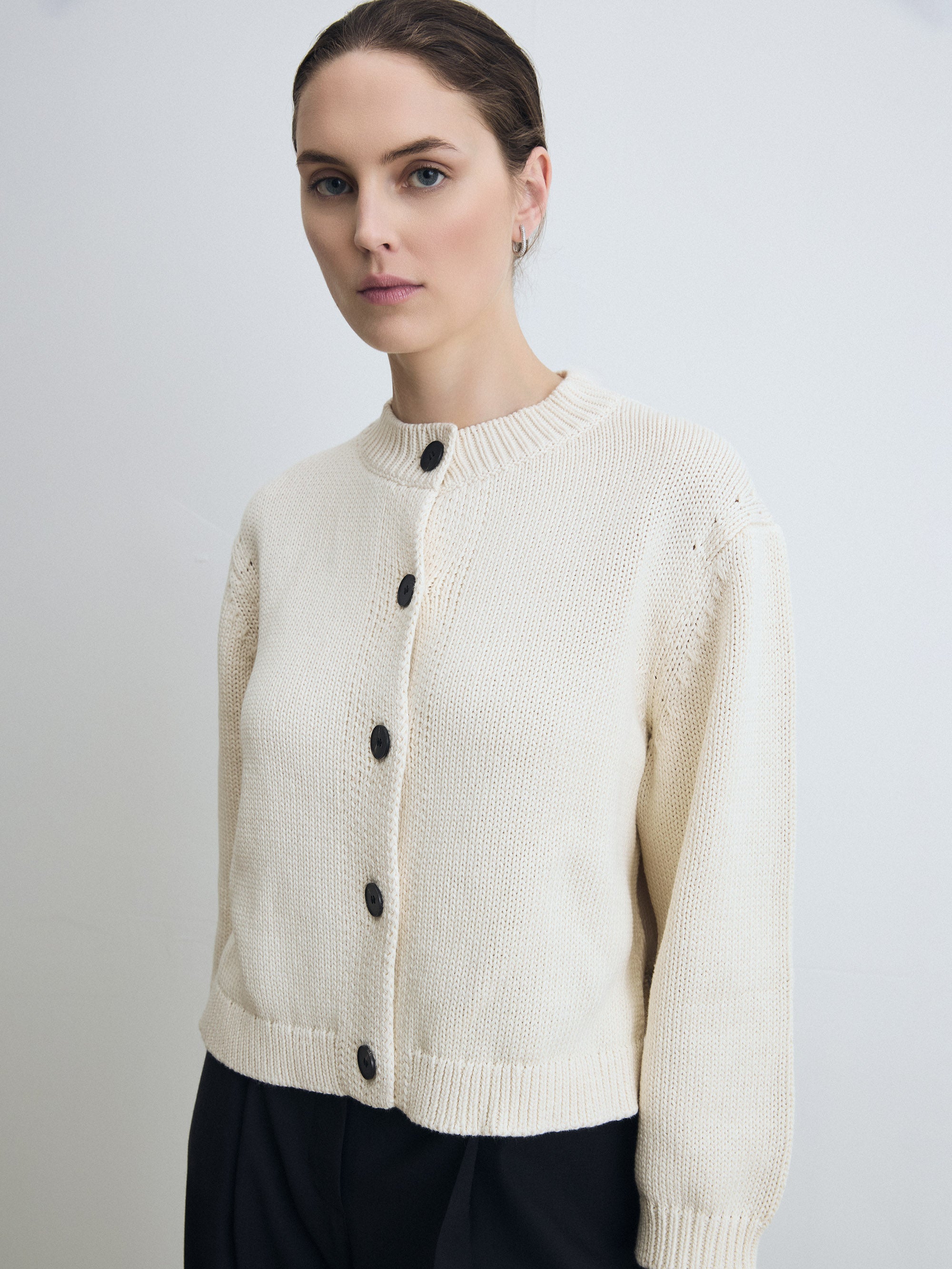 Woman wearing a pearl cardigan with black buttons on a plain background