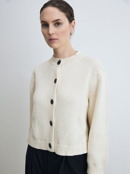 Woman wearing a pearl cardigan with black buttons on a plain background
