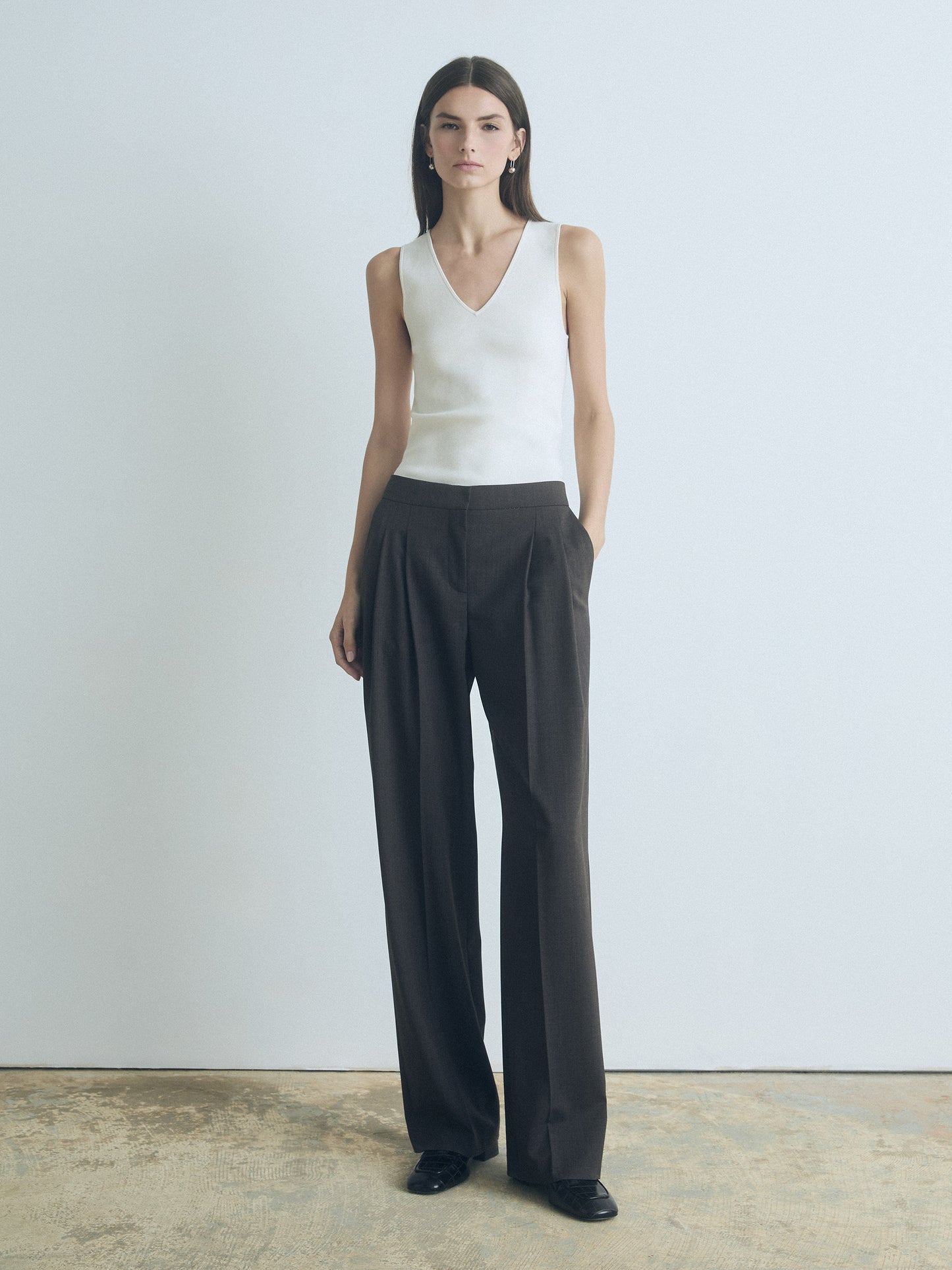 Woman wearing a white sleeveless top and black wide-leg pants against a plain background