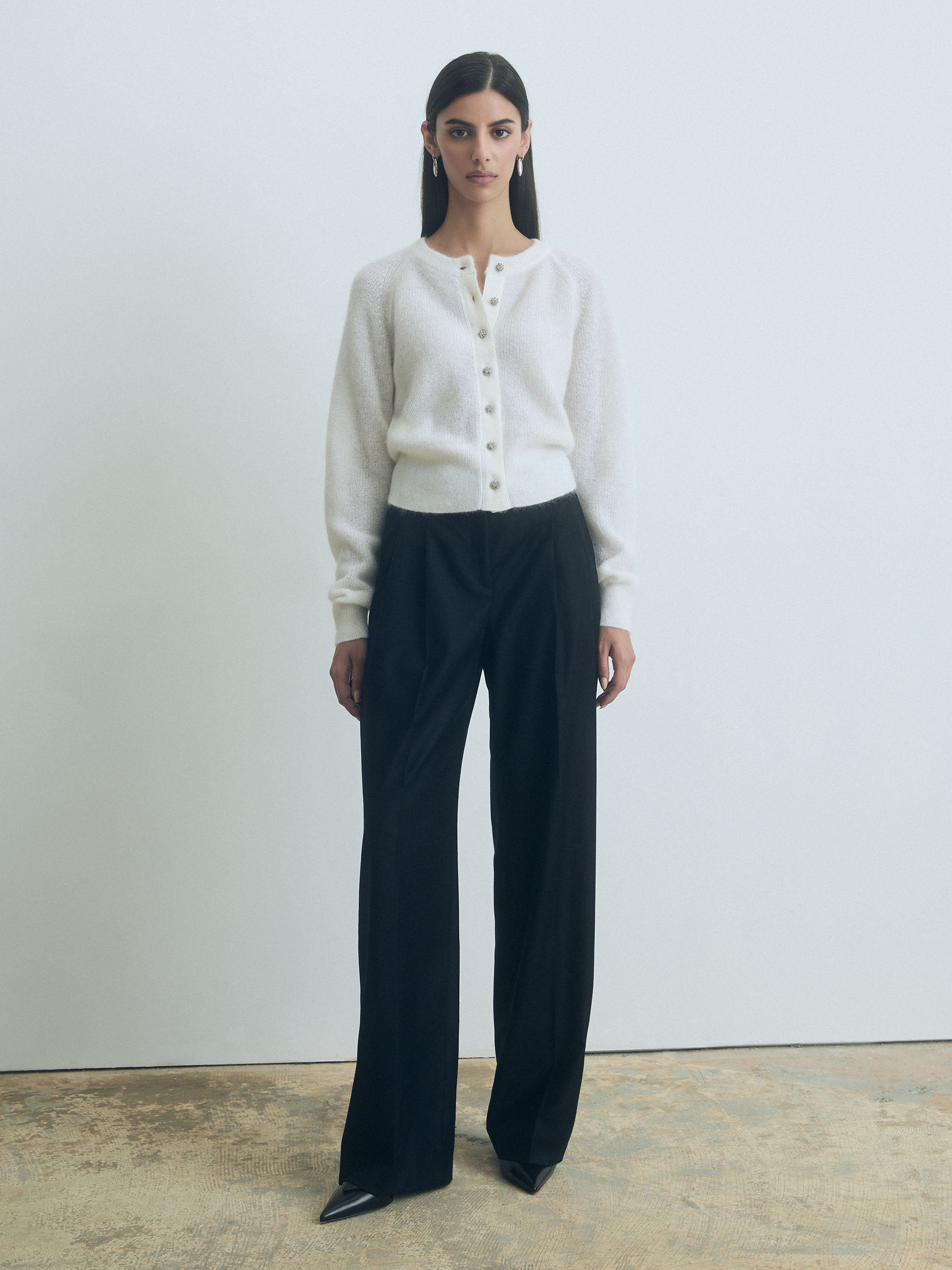 Woman wearing a white judith and charles cardigan embellished front button closure and black pants against a plain background