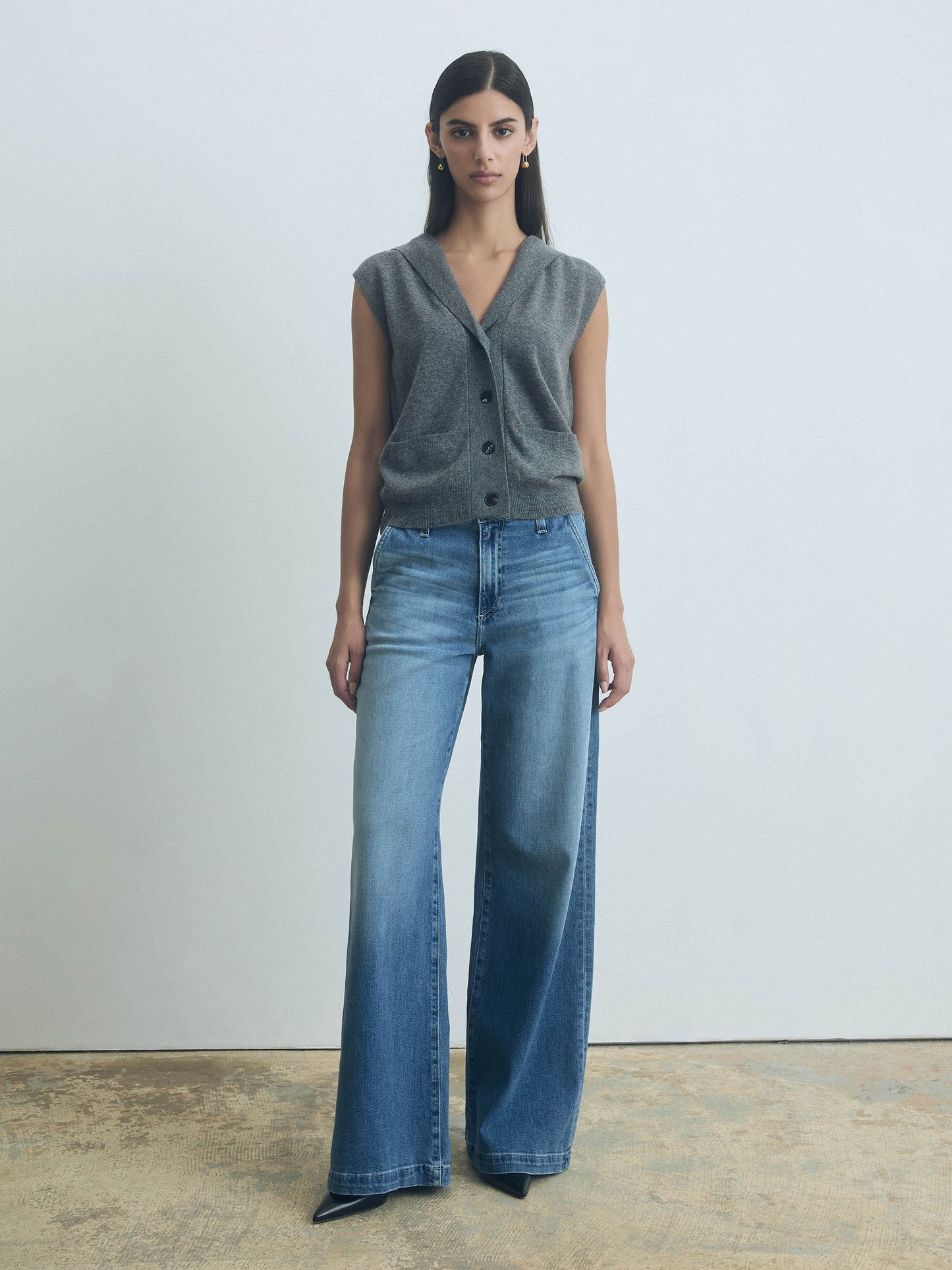 Woman wearing a Grey Melange sleeveless hooded wool-cashmere vest with button front closure by Judith & Charles and blue jeans against a plain background