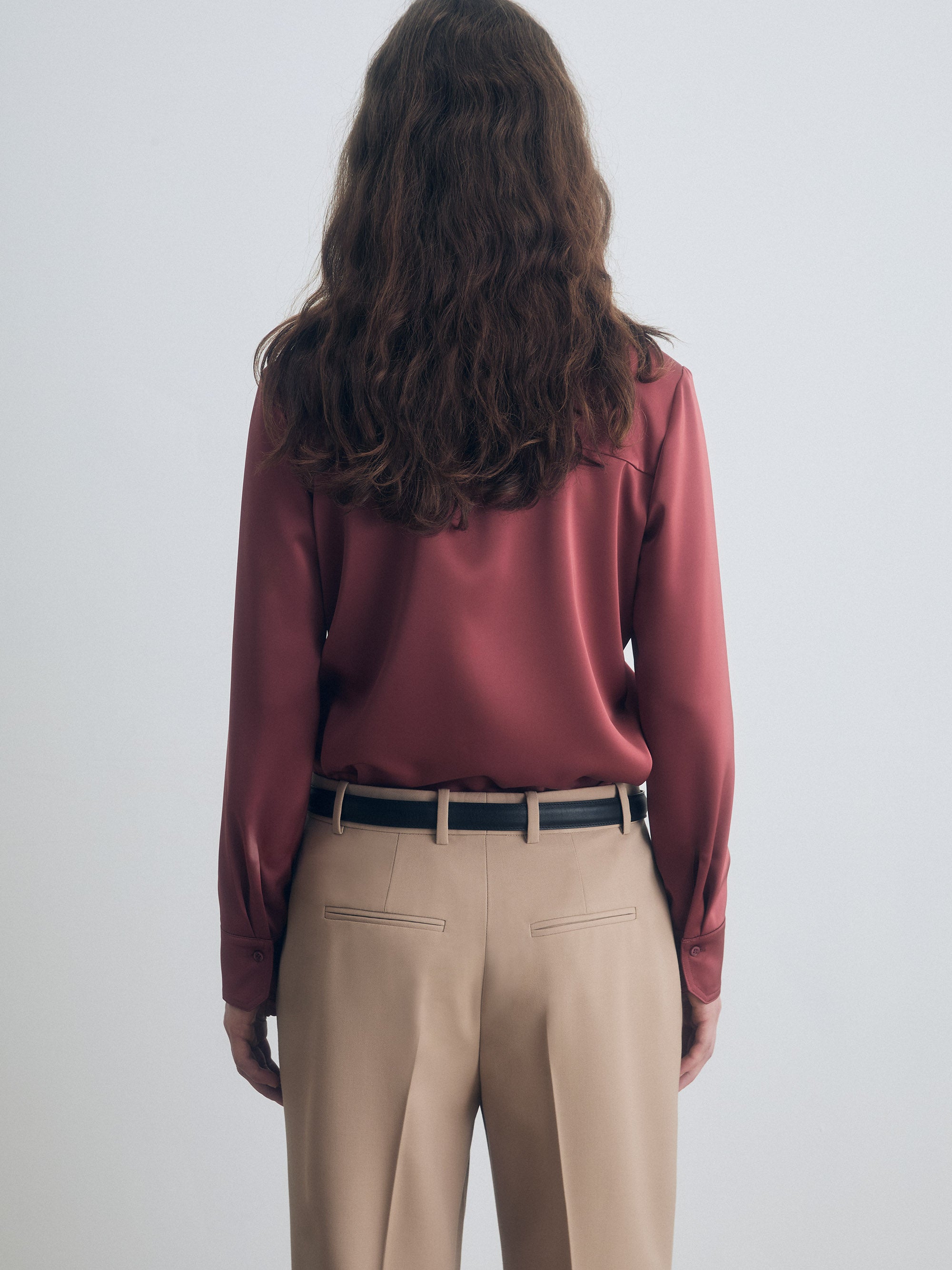 Person wearing a terracotta blouse and beige pants against a white background