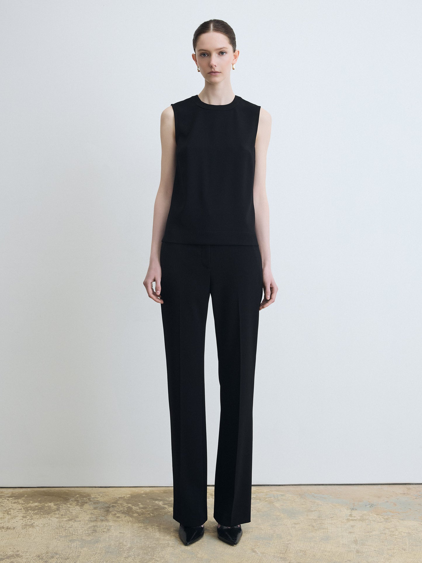 Person wearing a black sleeveless top and black pants on a plain background