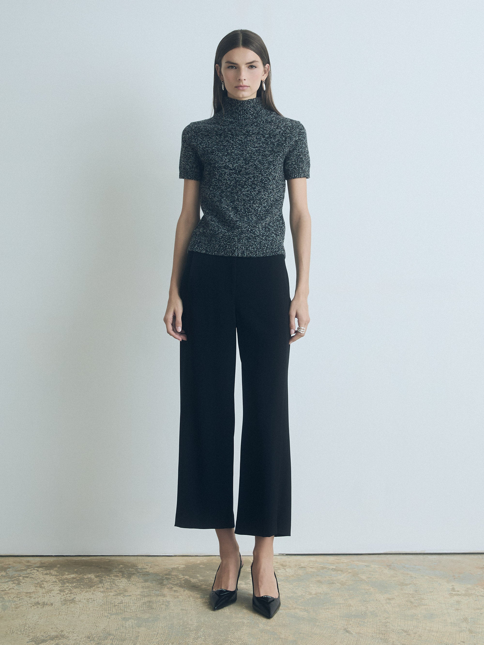 Woman wearing a patterned turtleneck and black wide-leg pants against a plain background