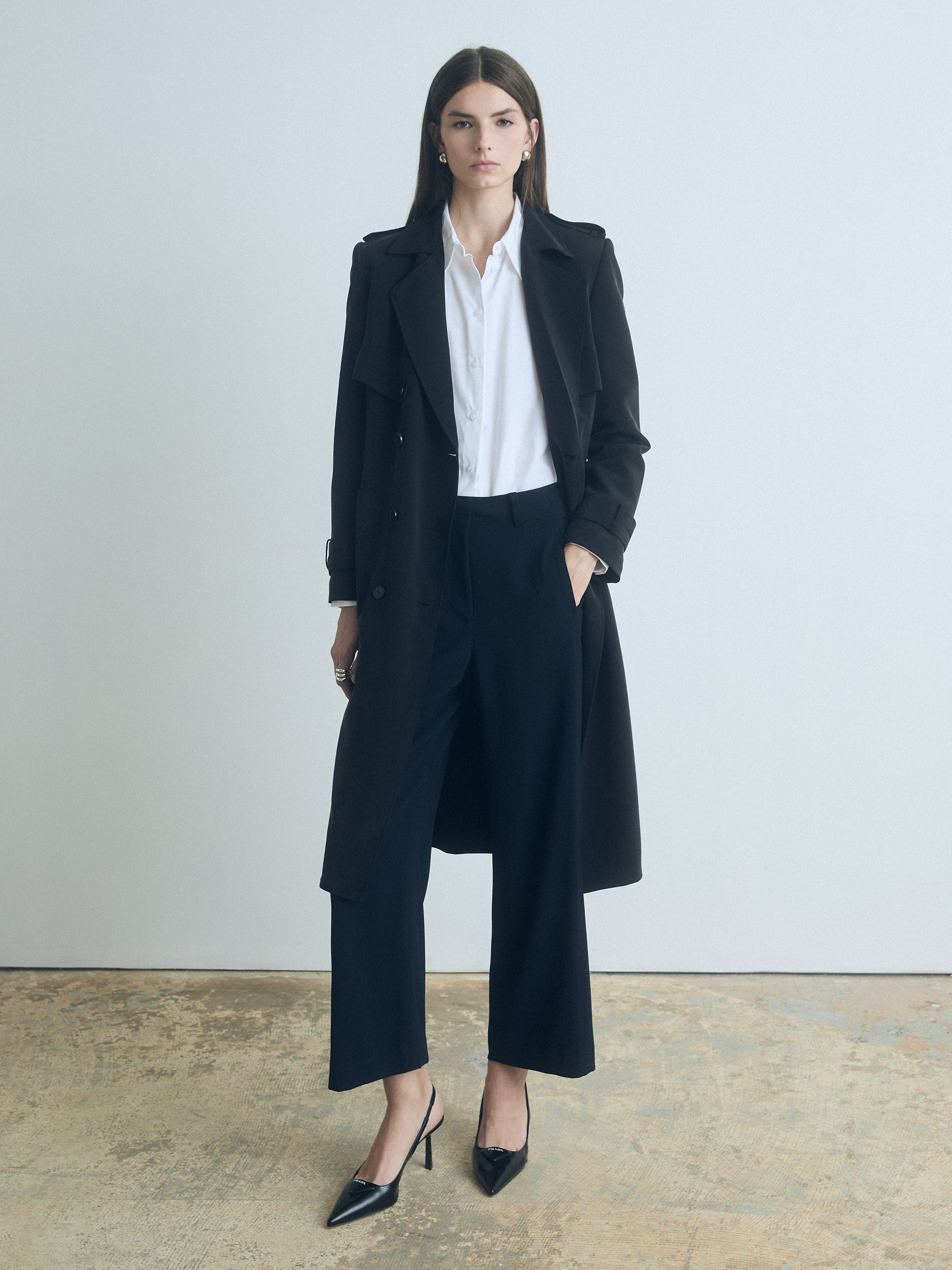 Model wearing Judith & Charles navy Laurel pants styled with a white button-up shirt, black trench coat, and black heels