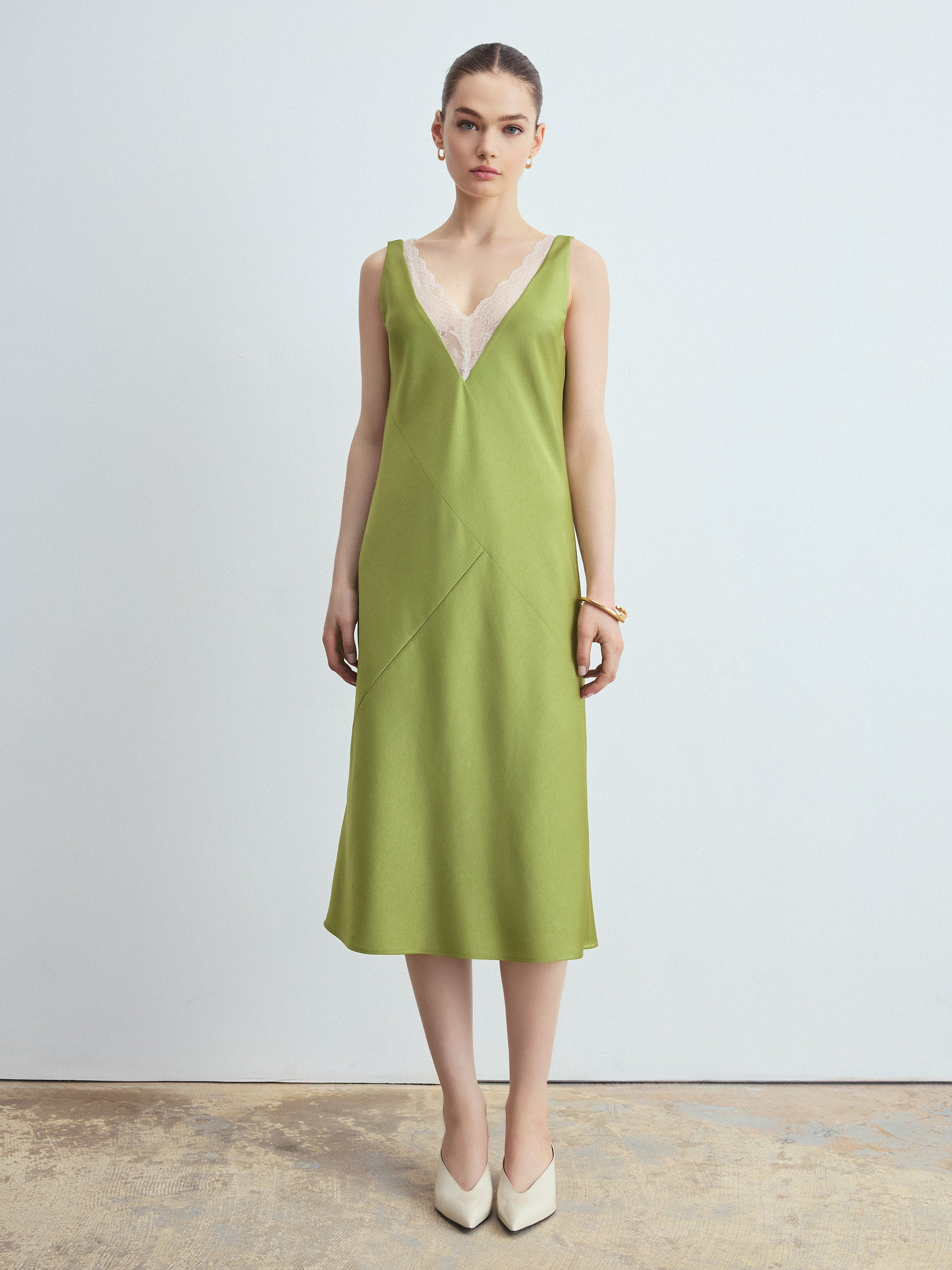 Woman wearing a green slip dress with a white lace overlay against a plain background