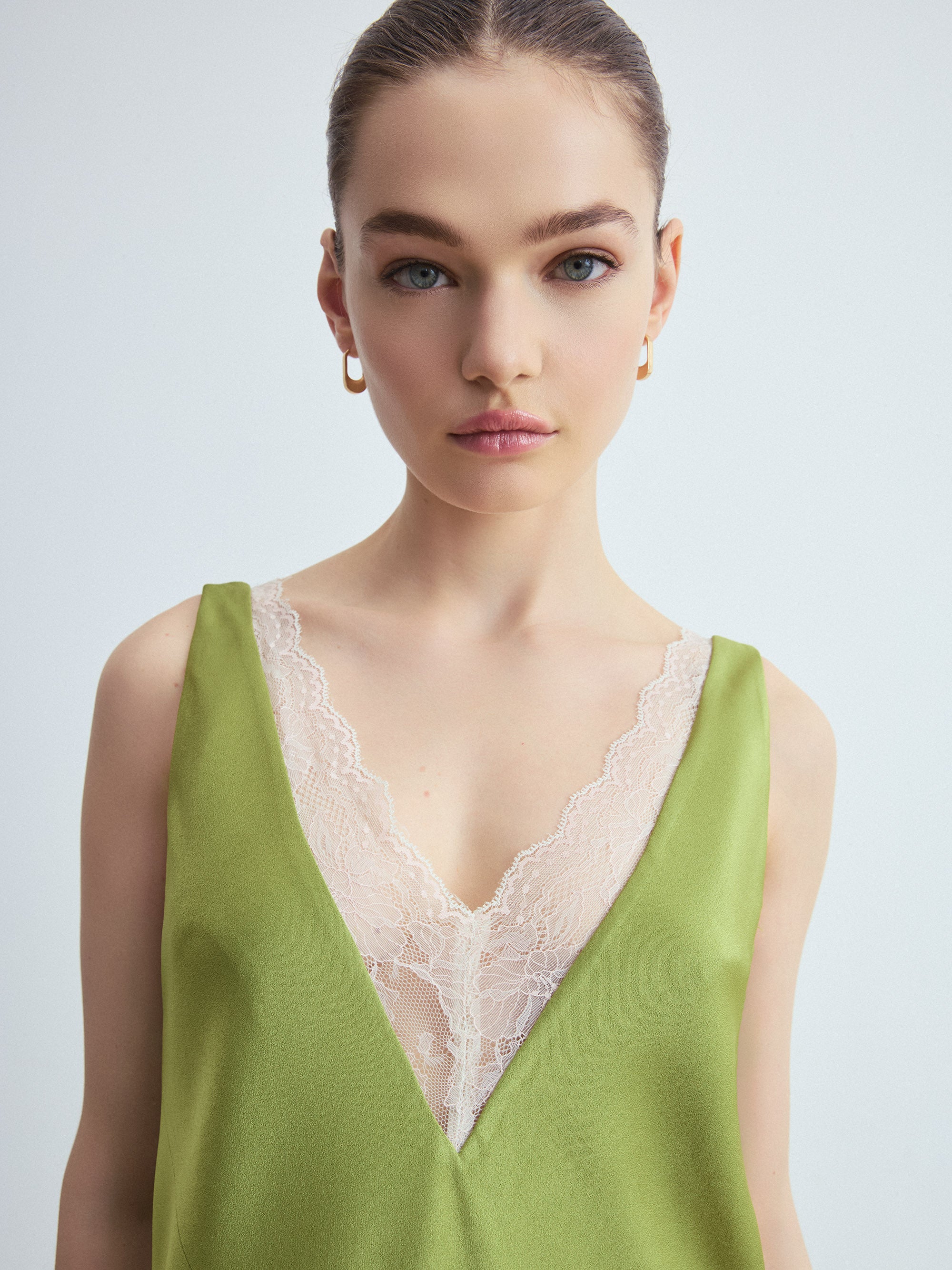 Woman wearing a green sleeveless dress with lace detail on a light gray background
