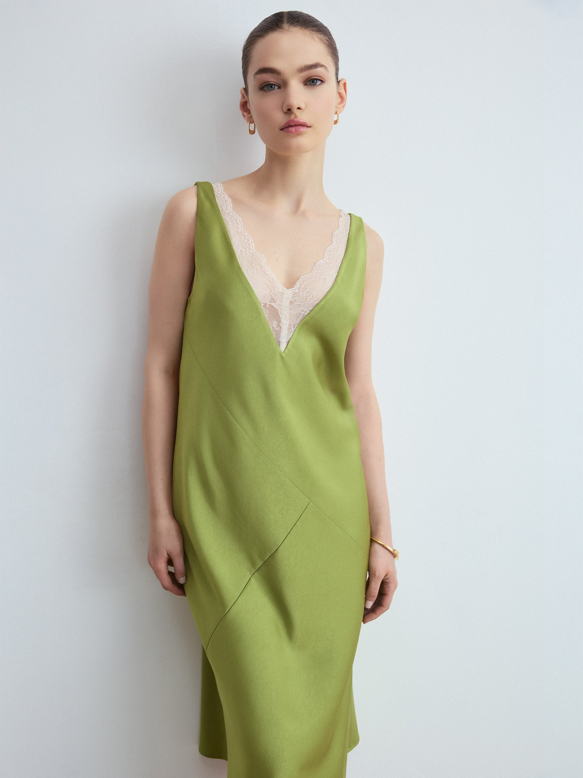 Woman wearing a green slip dress with a white lace overlay against a plain background