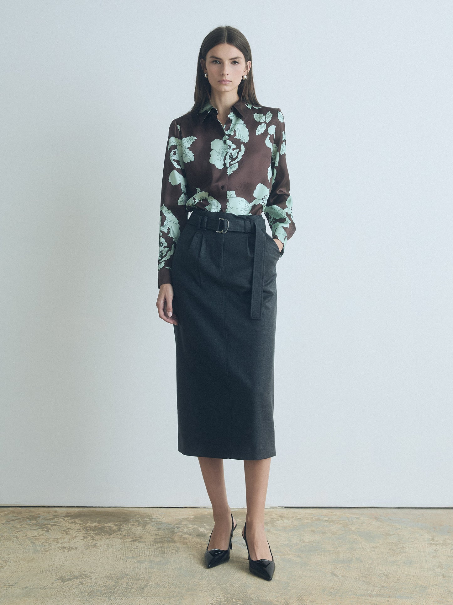 Woman wearing a floral blouse and black judith and charles skirt against a plain background