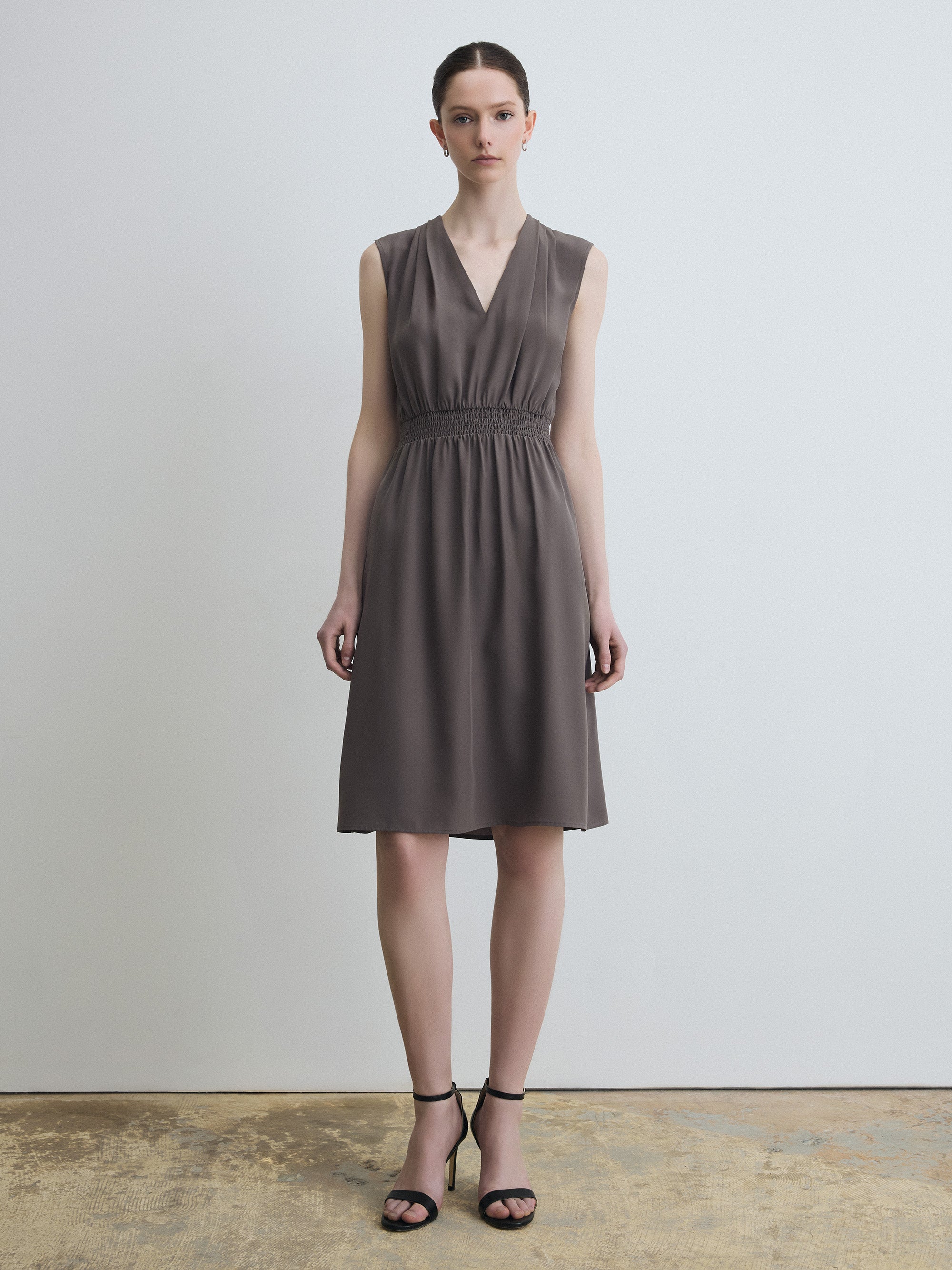 Woman wearing a sleeveless grey dress against a plain background