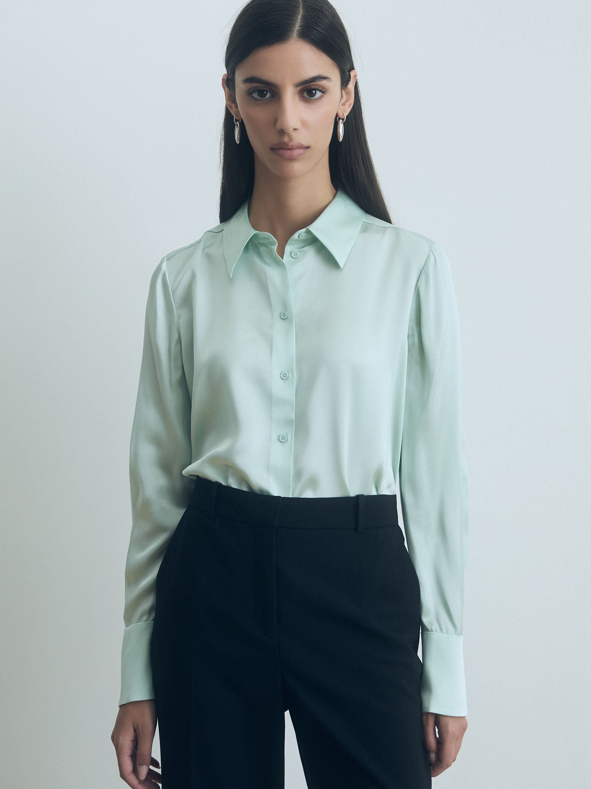 Woman wearing a light sage judith and charles and black pants against a plain background