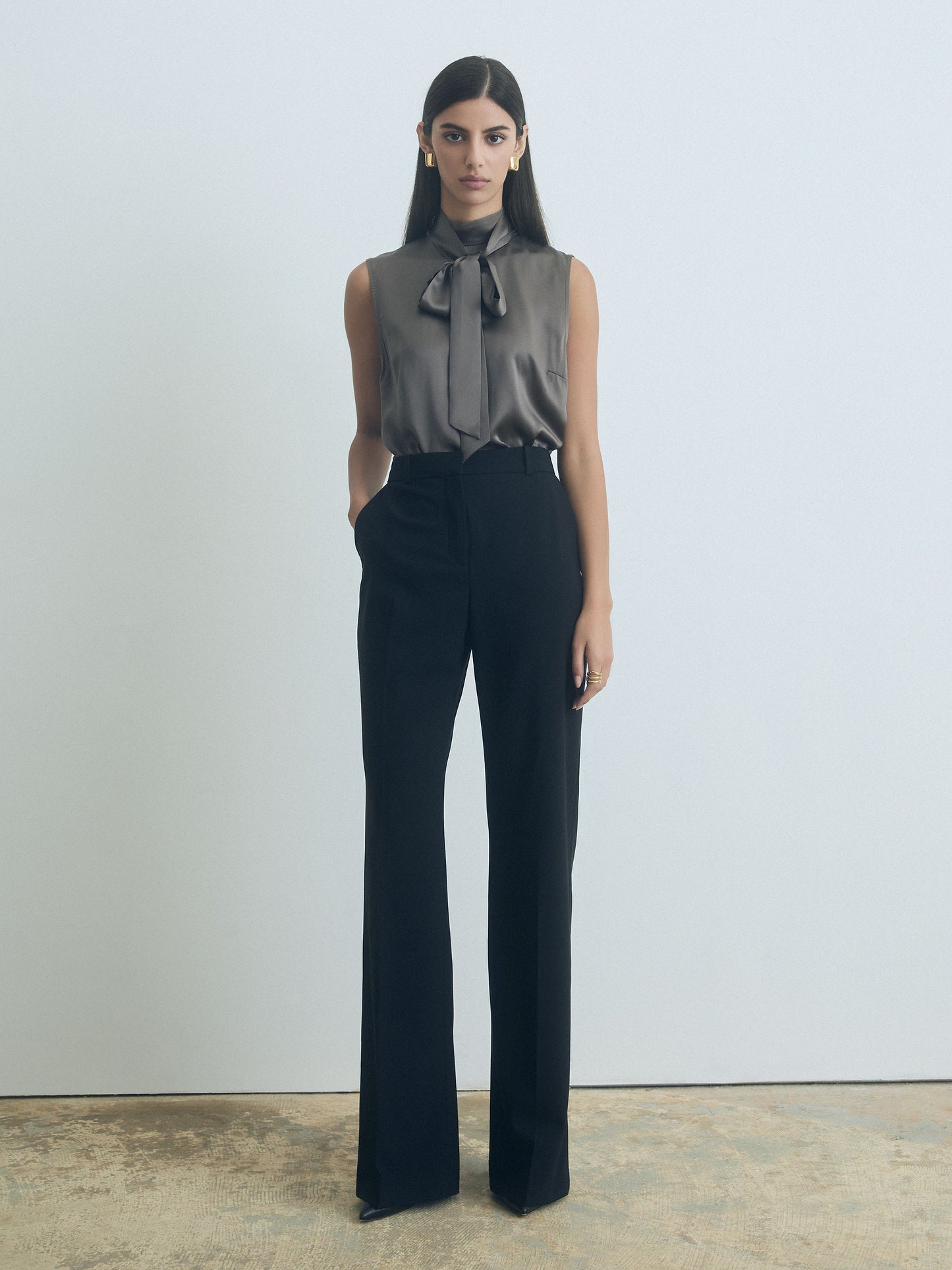 Woman wearing a sleeveless judith and charles top with a bow and dark pants against a plain background