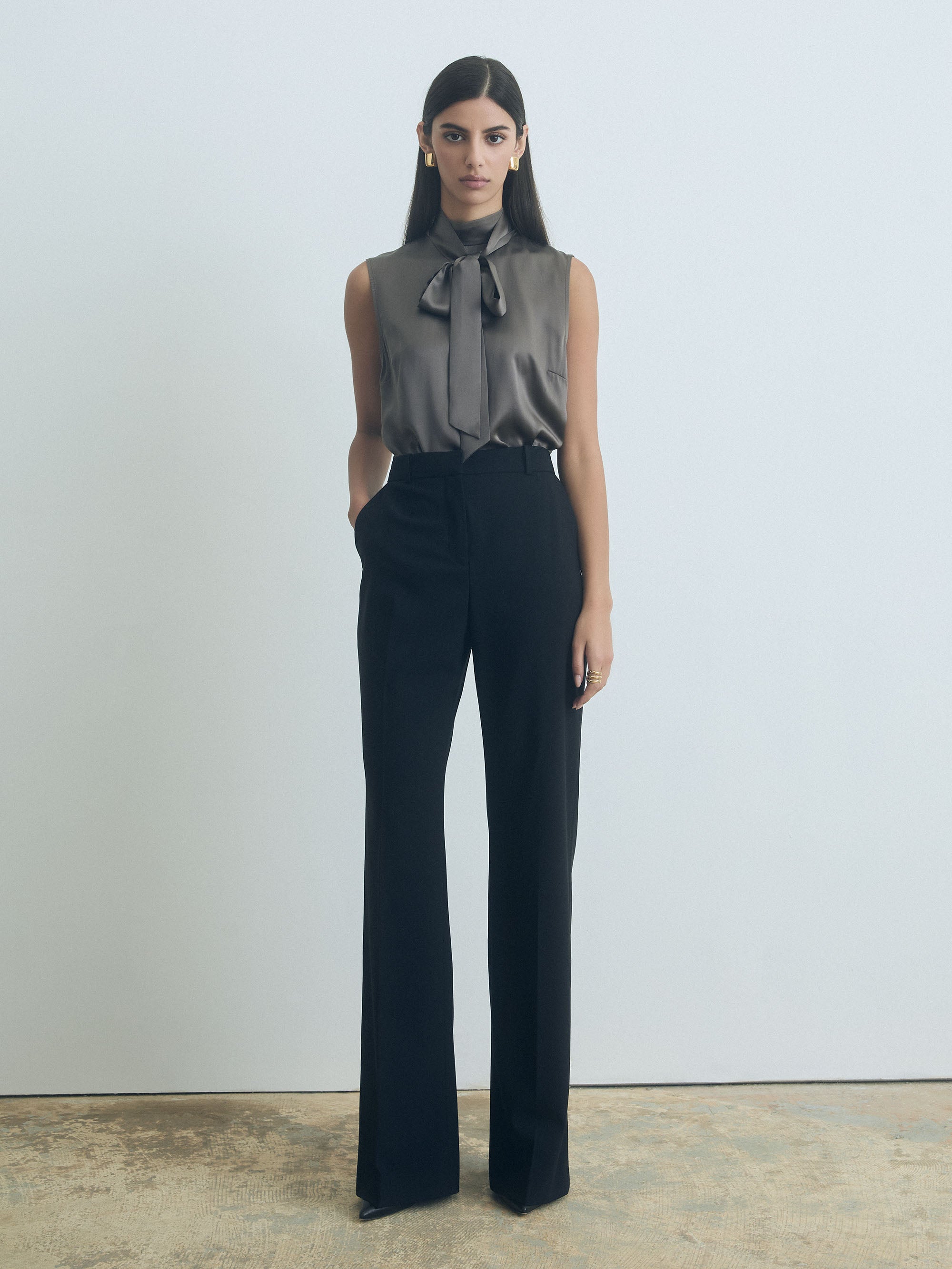 Woman wearing a sleeveless judith and charles top with a bow and dark pants against a plain background