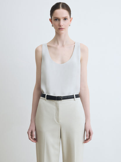 Woman wearing a white sleeveless top and beige pants on a plain background