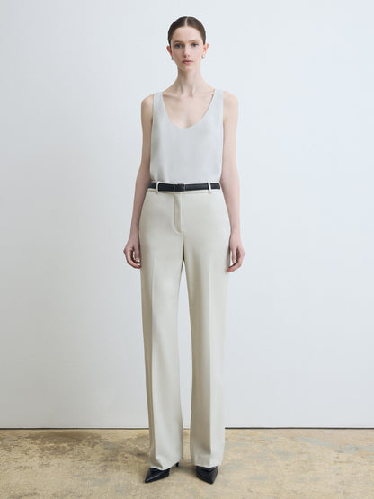 Woman wearing a white sleeveless top and beige pants against a plain background