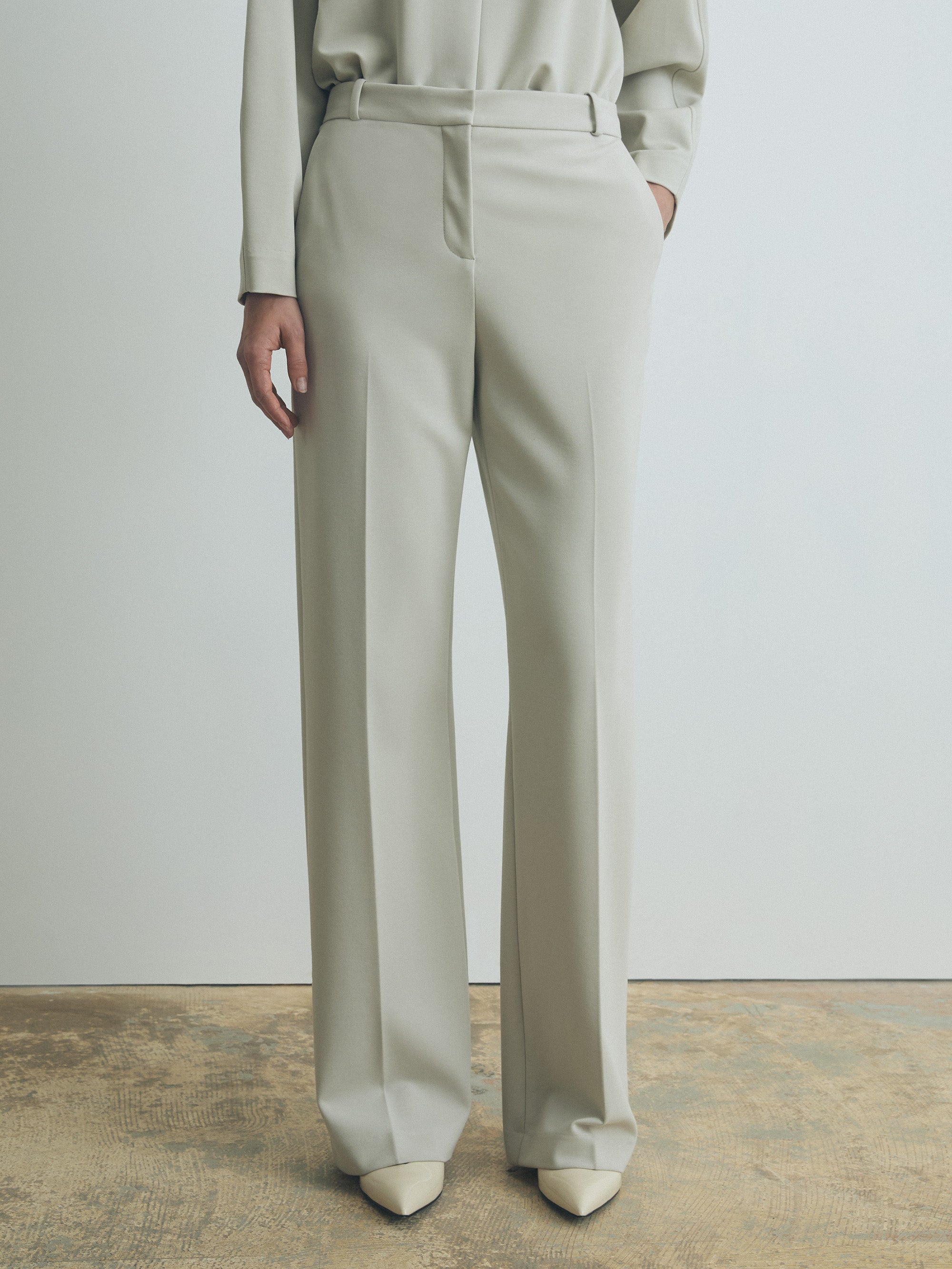 Person wearing light gray pants and a matching top against a plain background