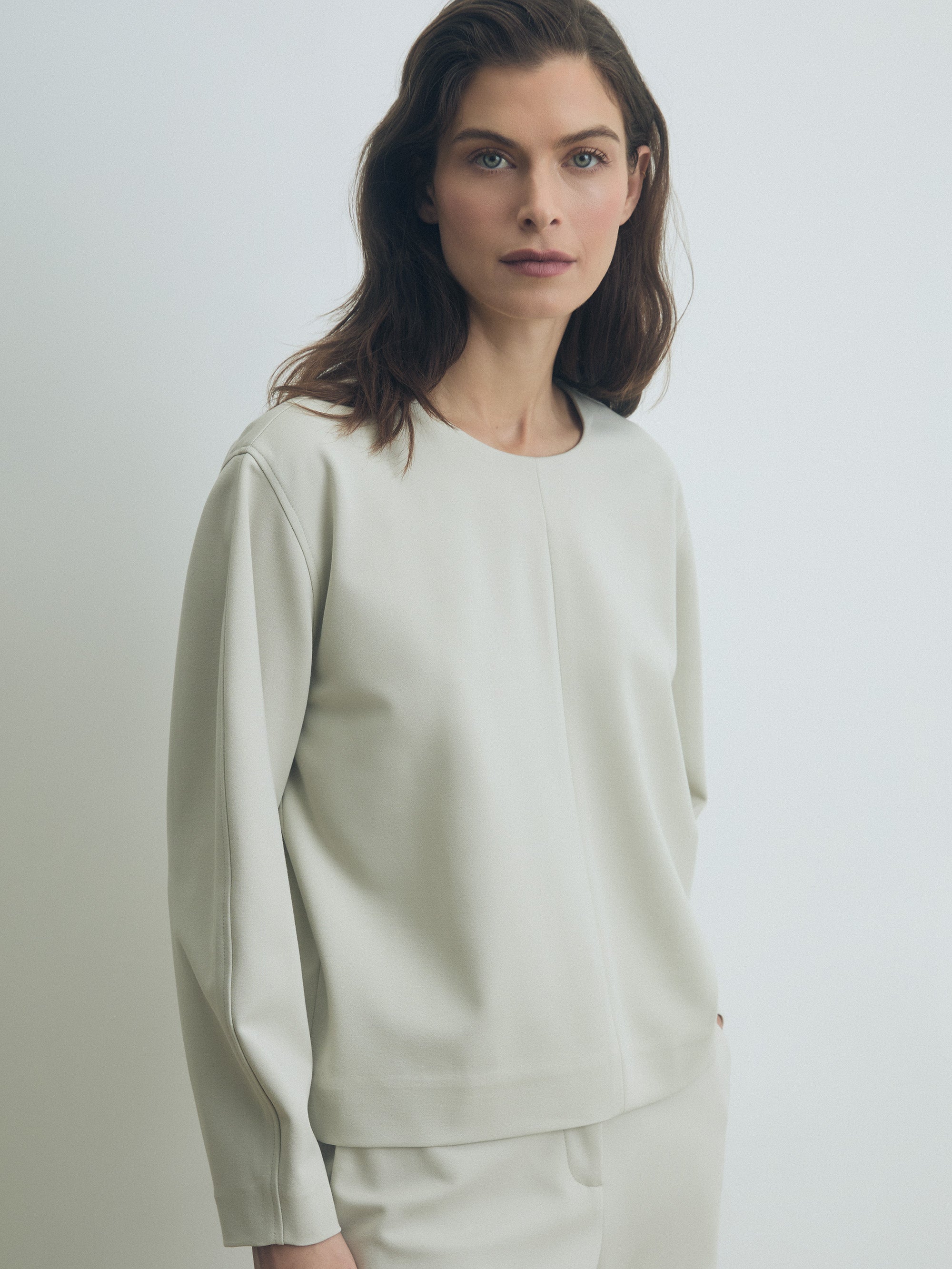 Woman wearing a light green long-sleeve top and pants on a white background