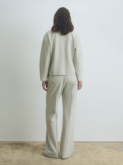 Person wearing a light gray suit standing against a white wall.