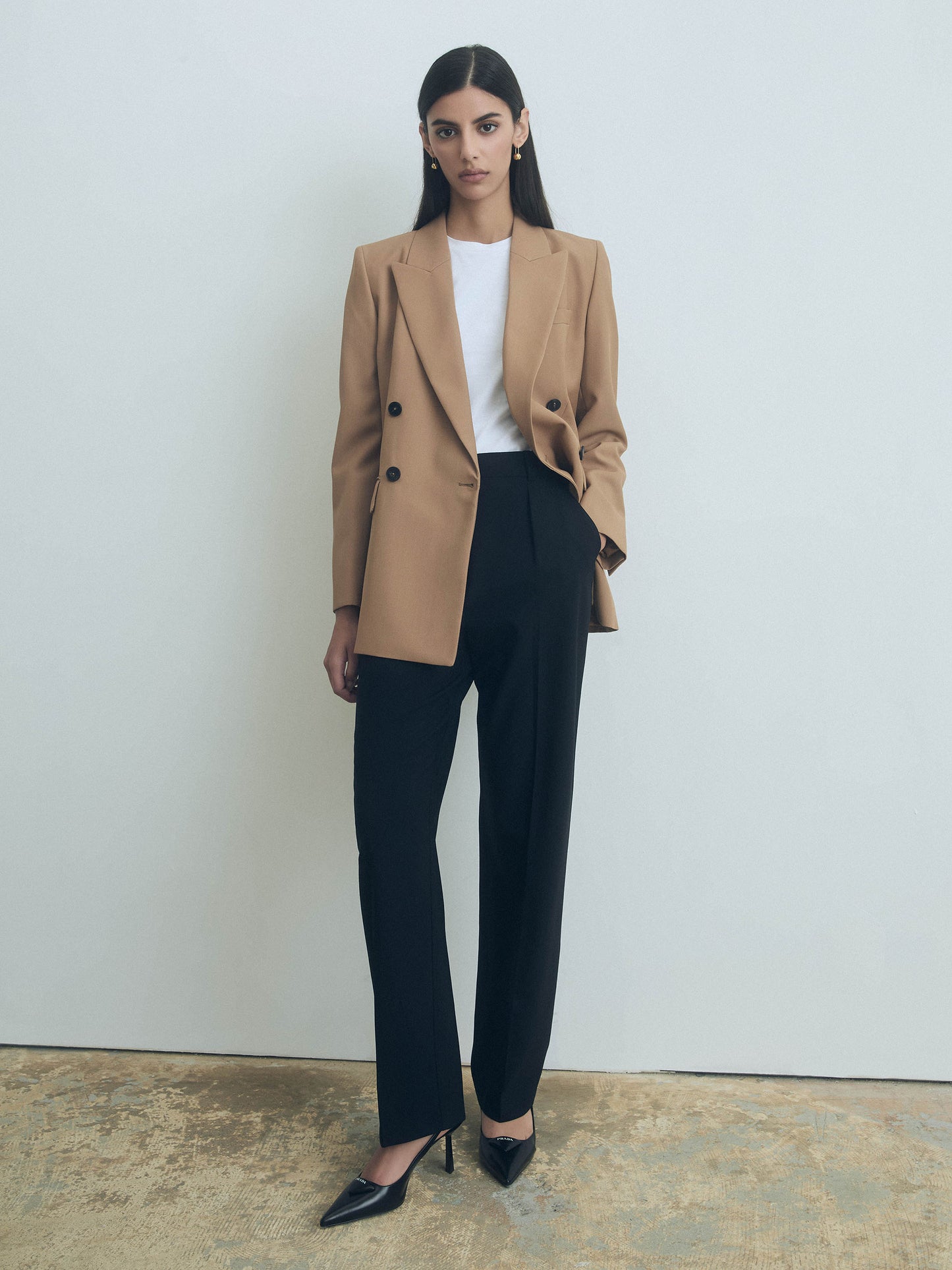 Woman wearing a camel blazer, white shirt, and black judith and charles pants against a plain background