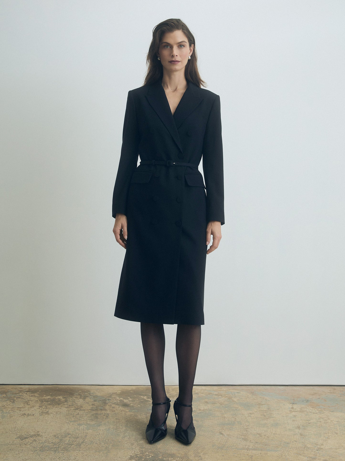 Woman wearing a black belted suit dress  against a plain background