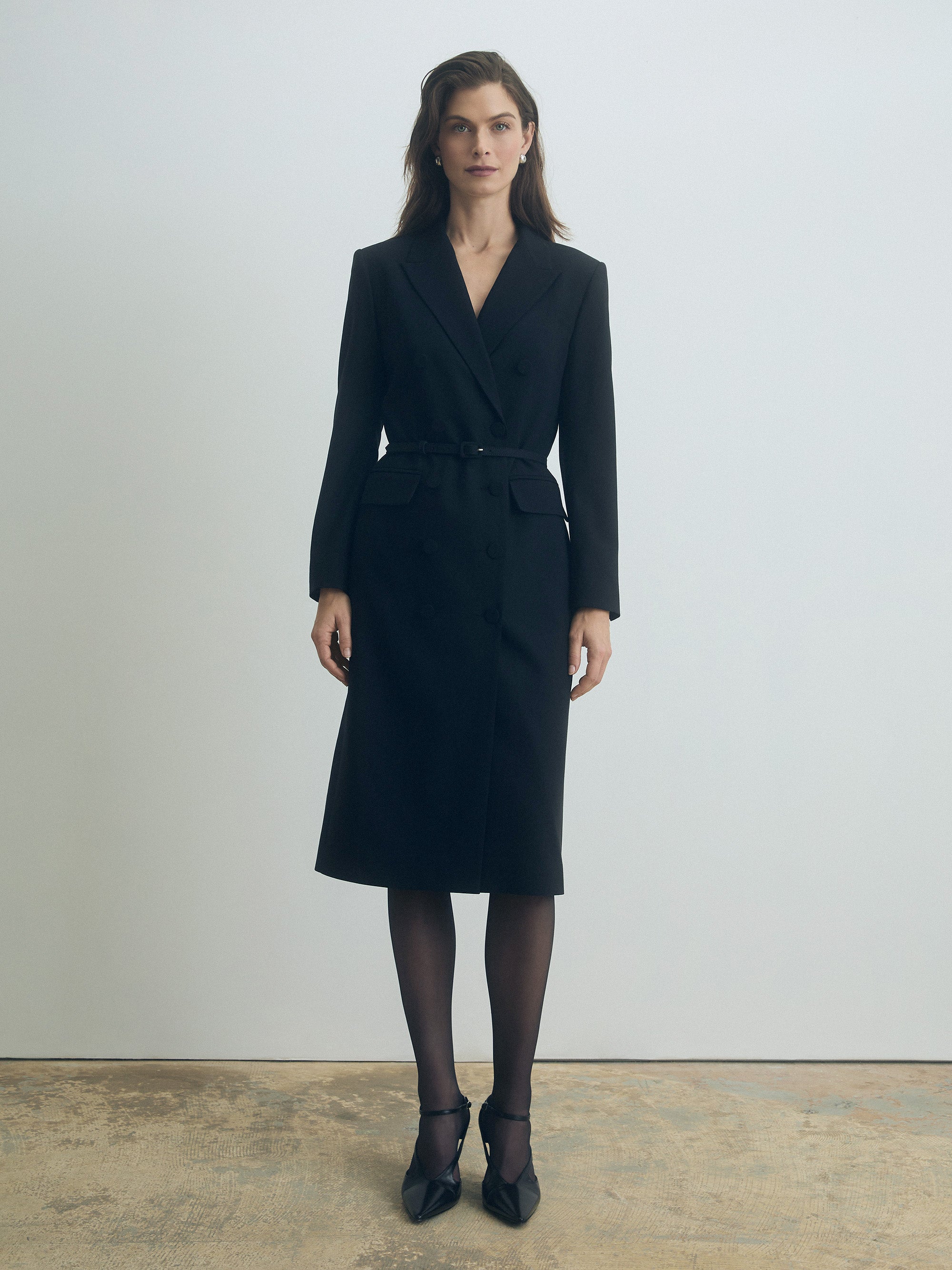 Woman wearing a black belted suit dress  against a plain background