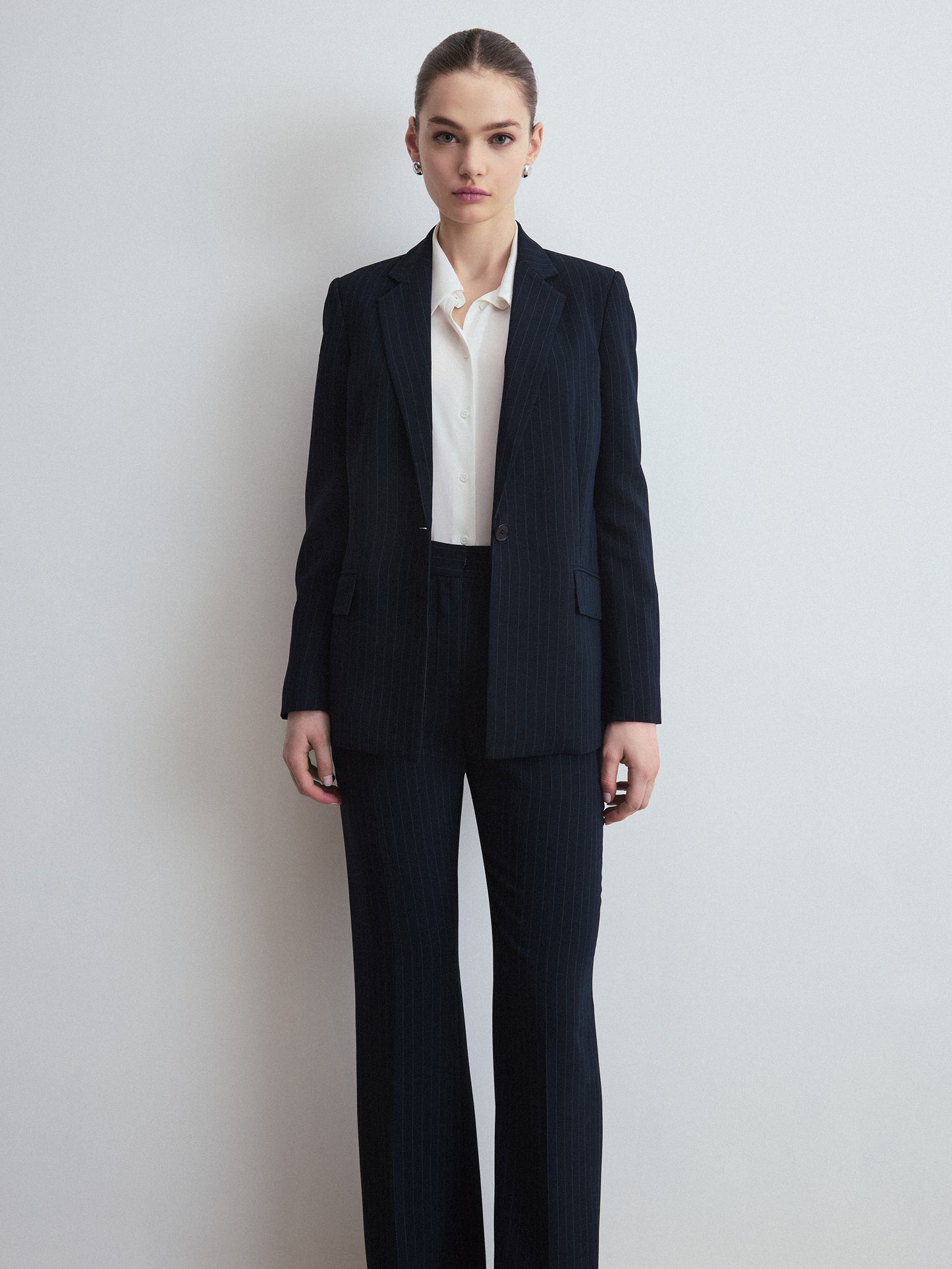 Person wearing a navy pinstripe suit with a white shirt on a light gray background