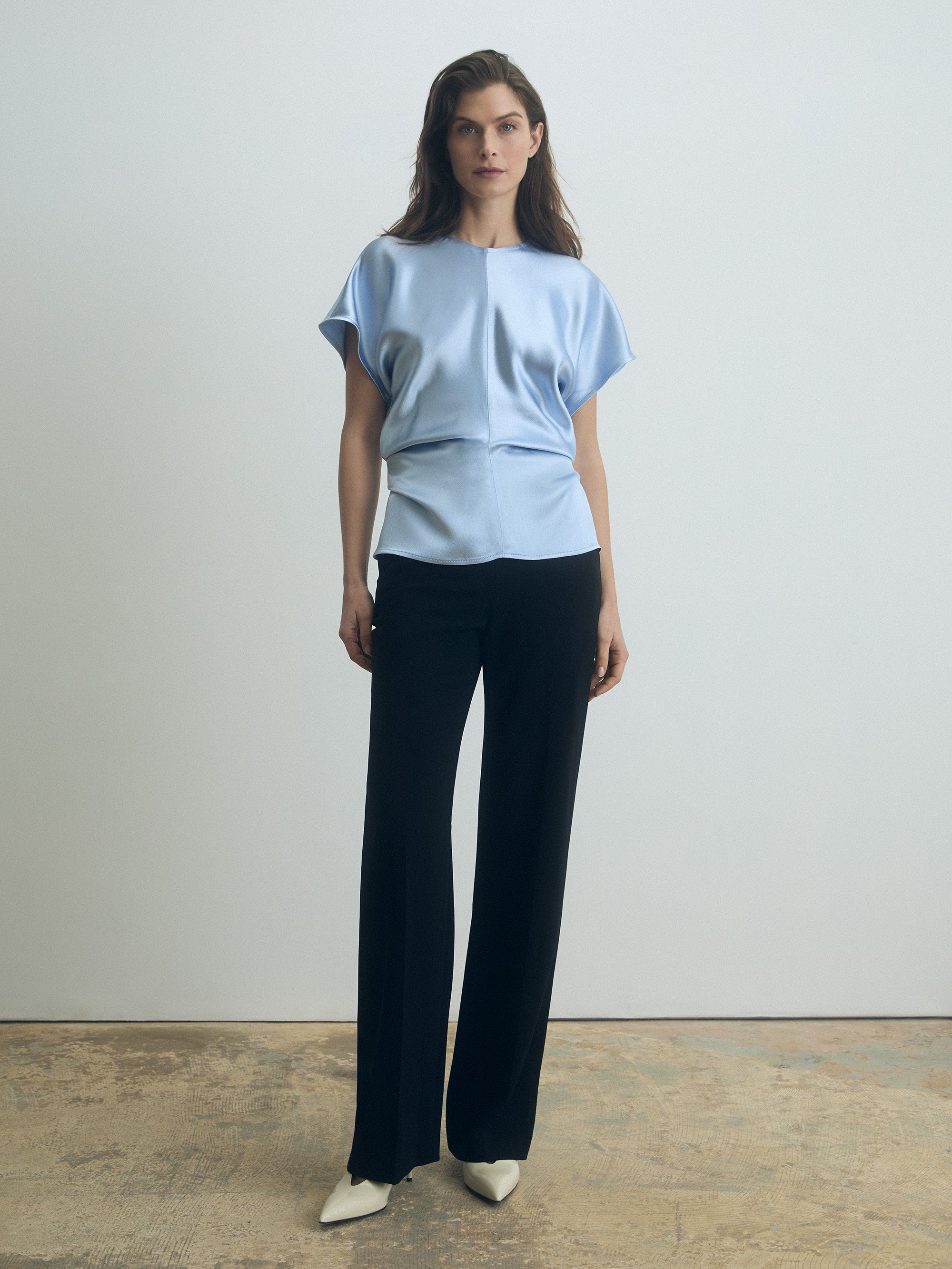Woman wearing a light textured satin glacial blue top and black pants against a plain background