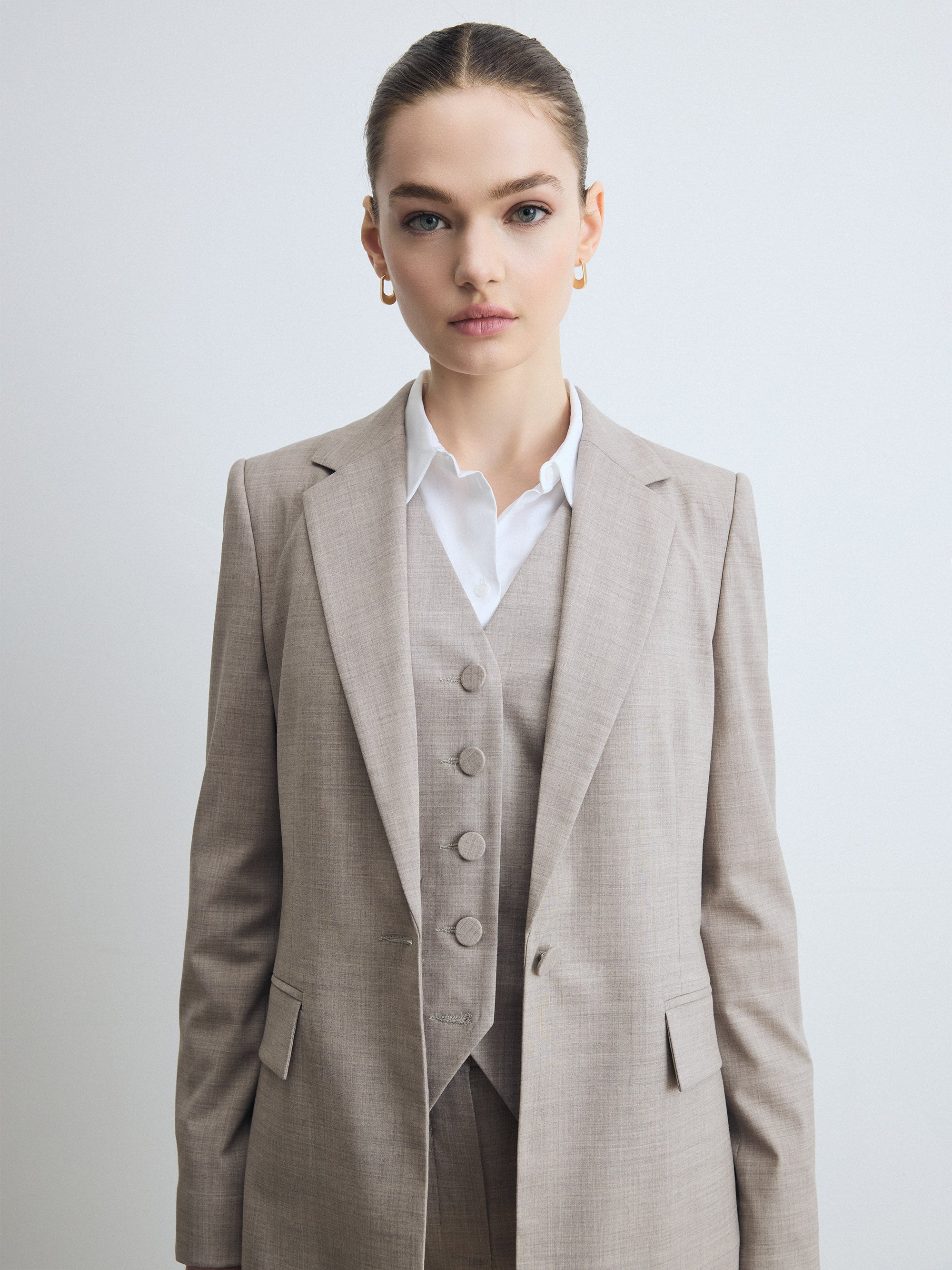 Close-up of a taupe melange tailored jacket worn over a matching buttoned waistcoat and white shirt, showing the notch lapel and flap pockets