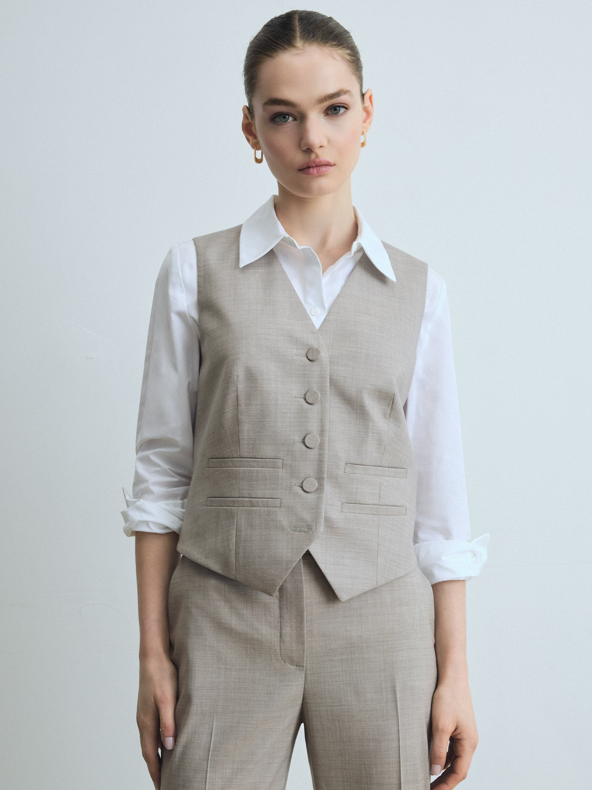 Woman wearing a taupe vest over a white shirt on a plain background