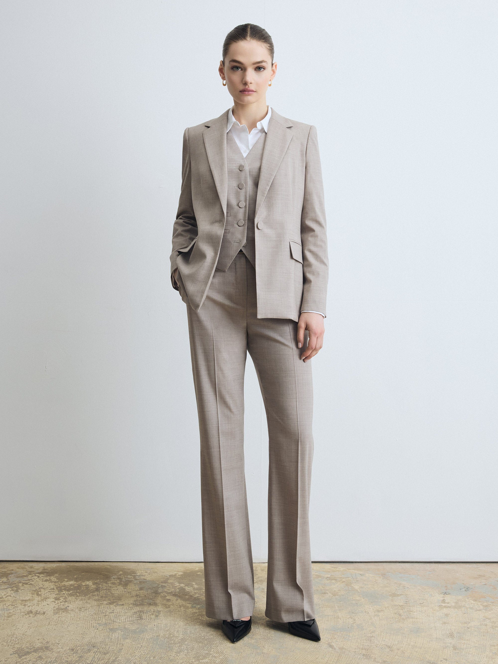 Tailored superfine Loro Piana merino fabric wool flare‑leg pant in taupe melange, shown styled with a matching blazer, vest, white shirt and pointed black shoes.