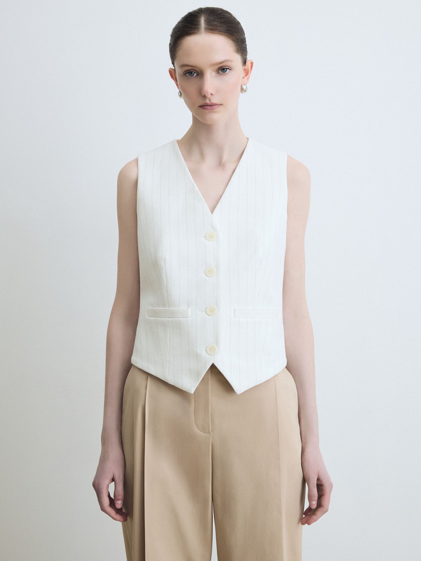 Woman wearing a white sleeveless vest over a beige pant on a light gray background