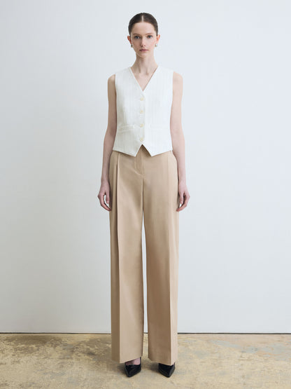 Woman wearing a white sleeveless top and beige pants against a plain background