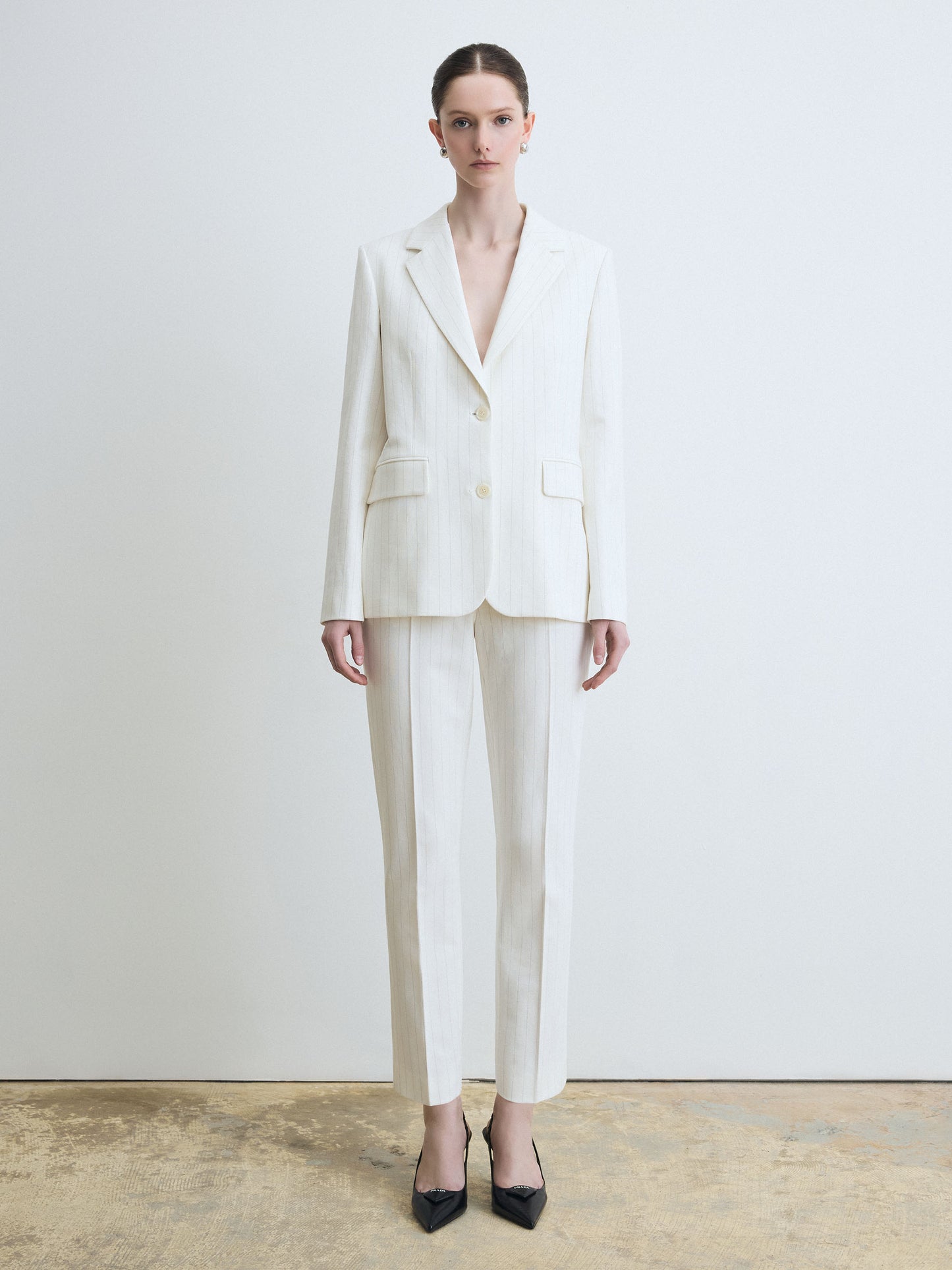 Woman wearing a white striped suit standing against a plain background