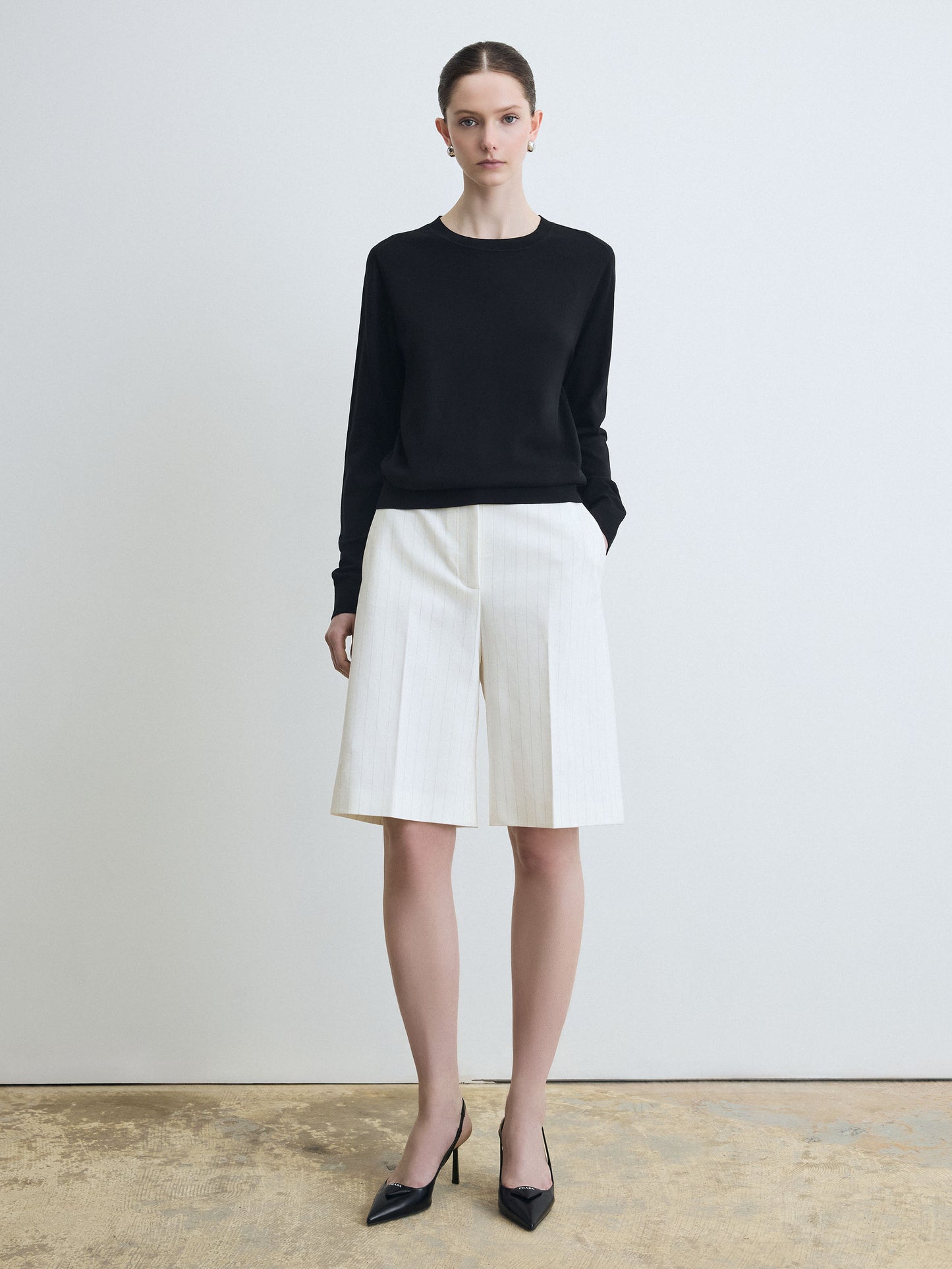 Woman wearing a black sweater and white shorts on a plain background